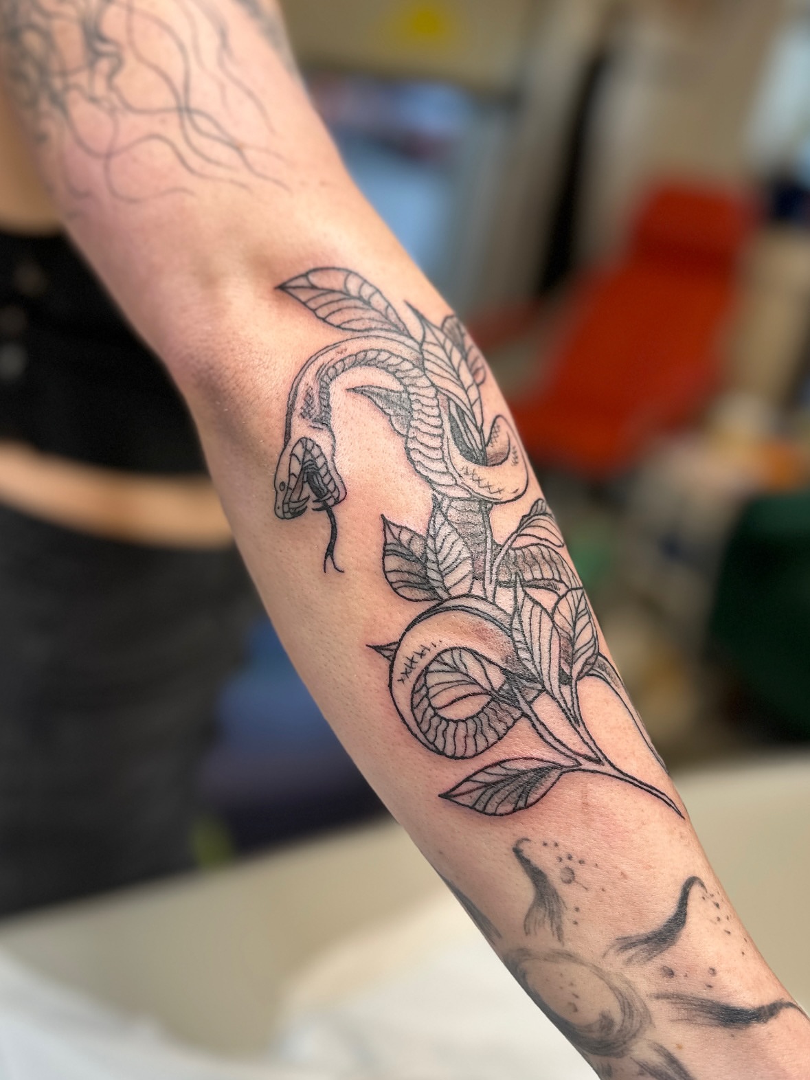 Snake and leaves black and grey tattoo on the forearm by Emma Berger
