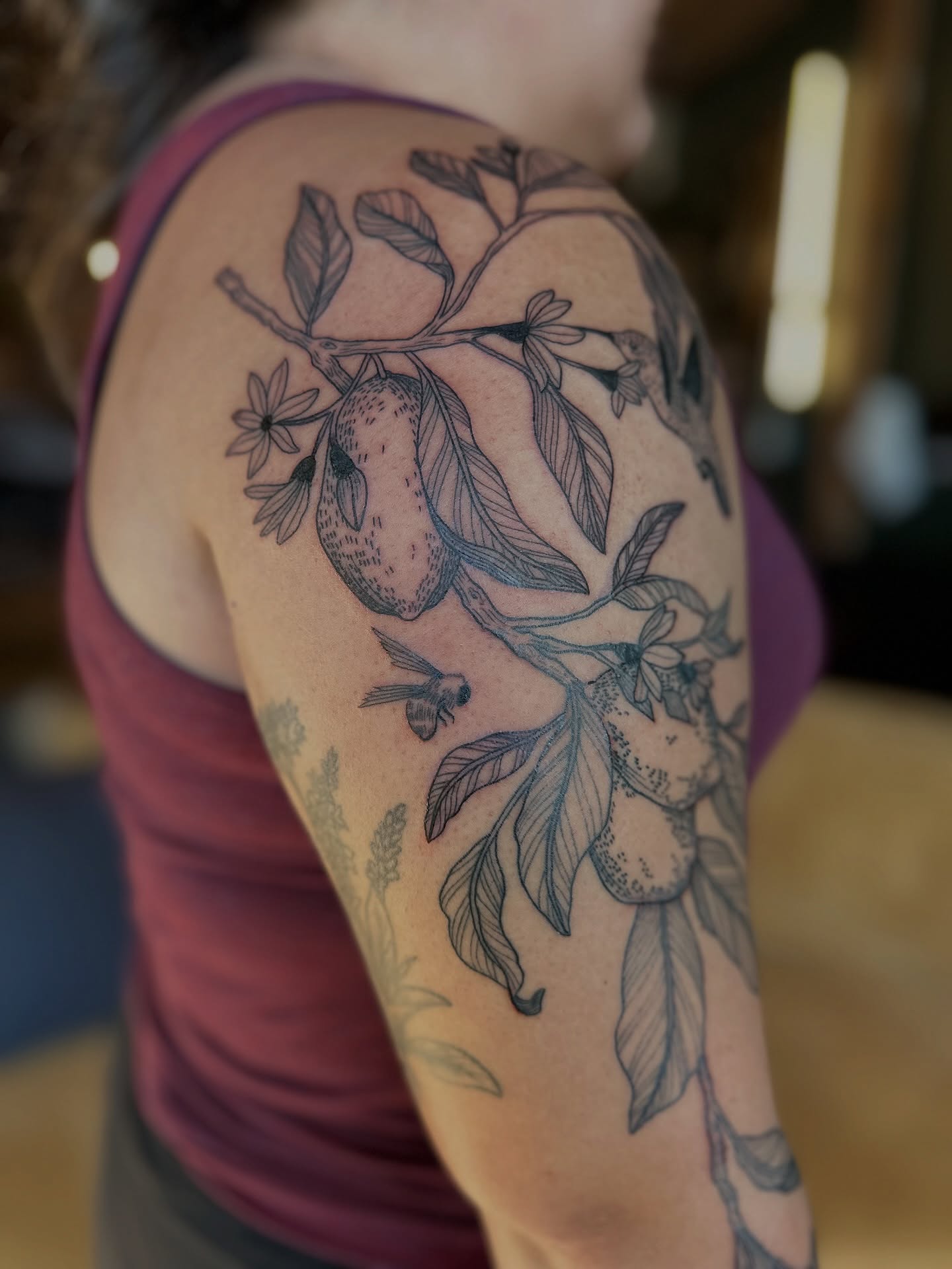 Branch with fruit and bee realism tattoo on the upper arm by Alexandra Gray