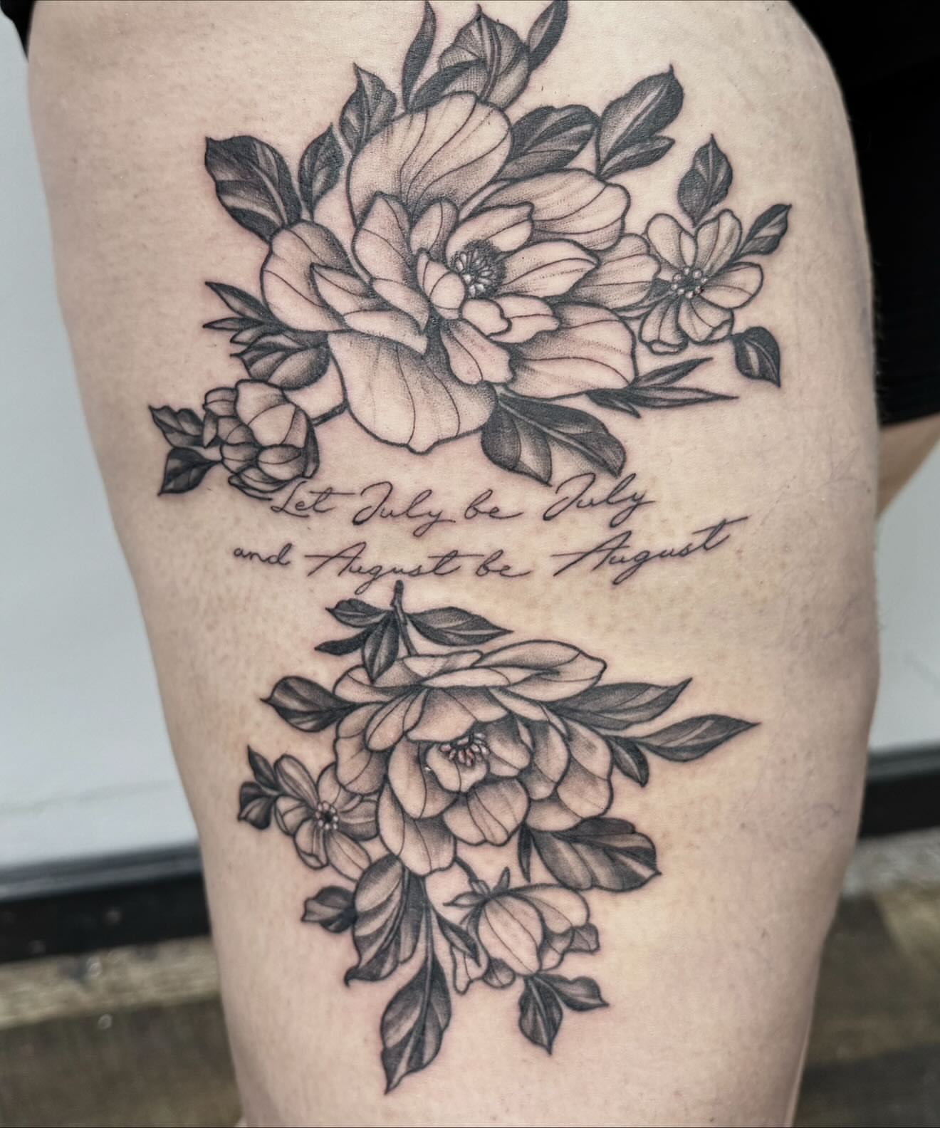 Flowers and quote black and grey tattoo on the thigh by Emmy