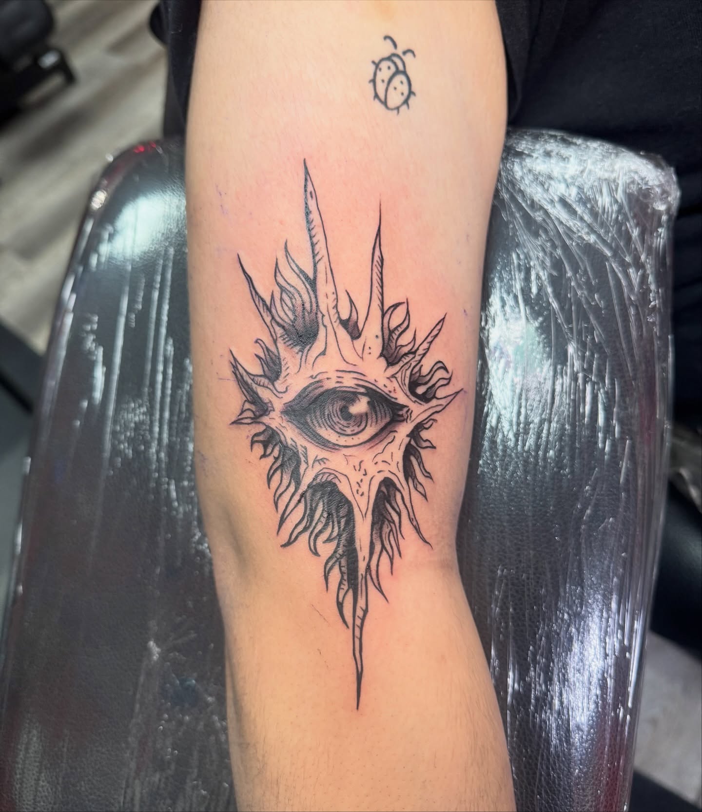 Eye with spikes black and grey tattoo on the forearm by Ryland - Tattoo Artist