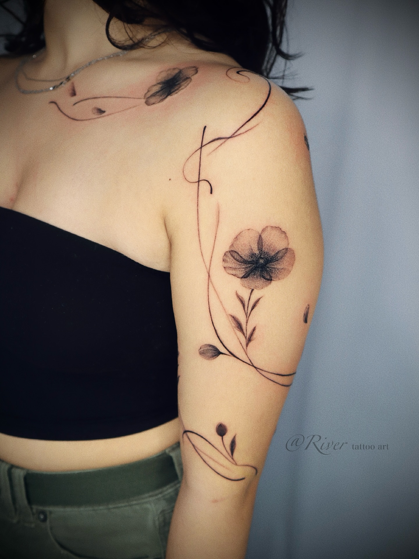 Flower and vine black and grey tattoo on the upper arm by River