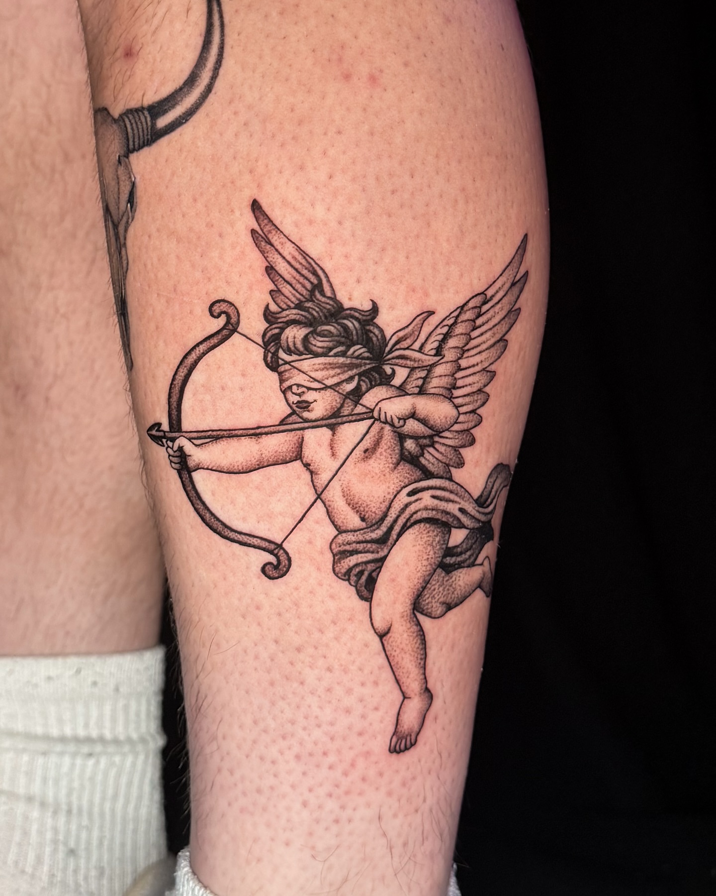 Cherub with bow black and grey tattoo on the thigh by Jae Traditional Tattoo