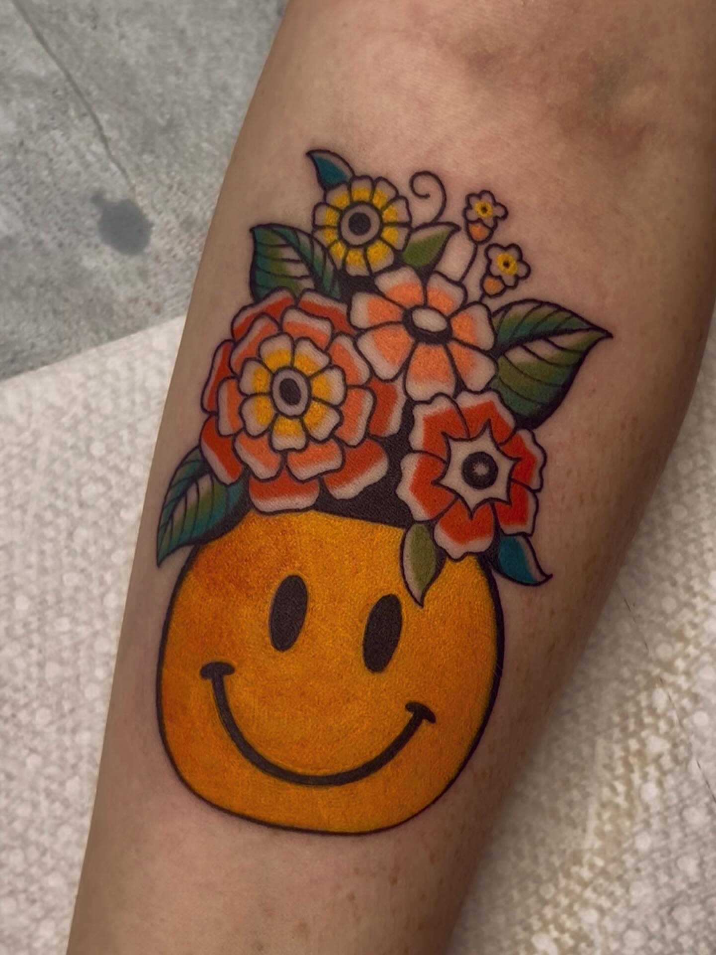 Smiley face with flowers American traditional tattoo on the forearm by ☻ darby robertson ☻