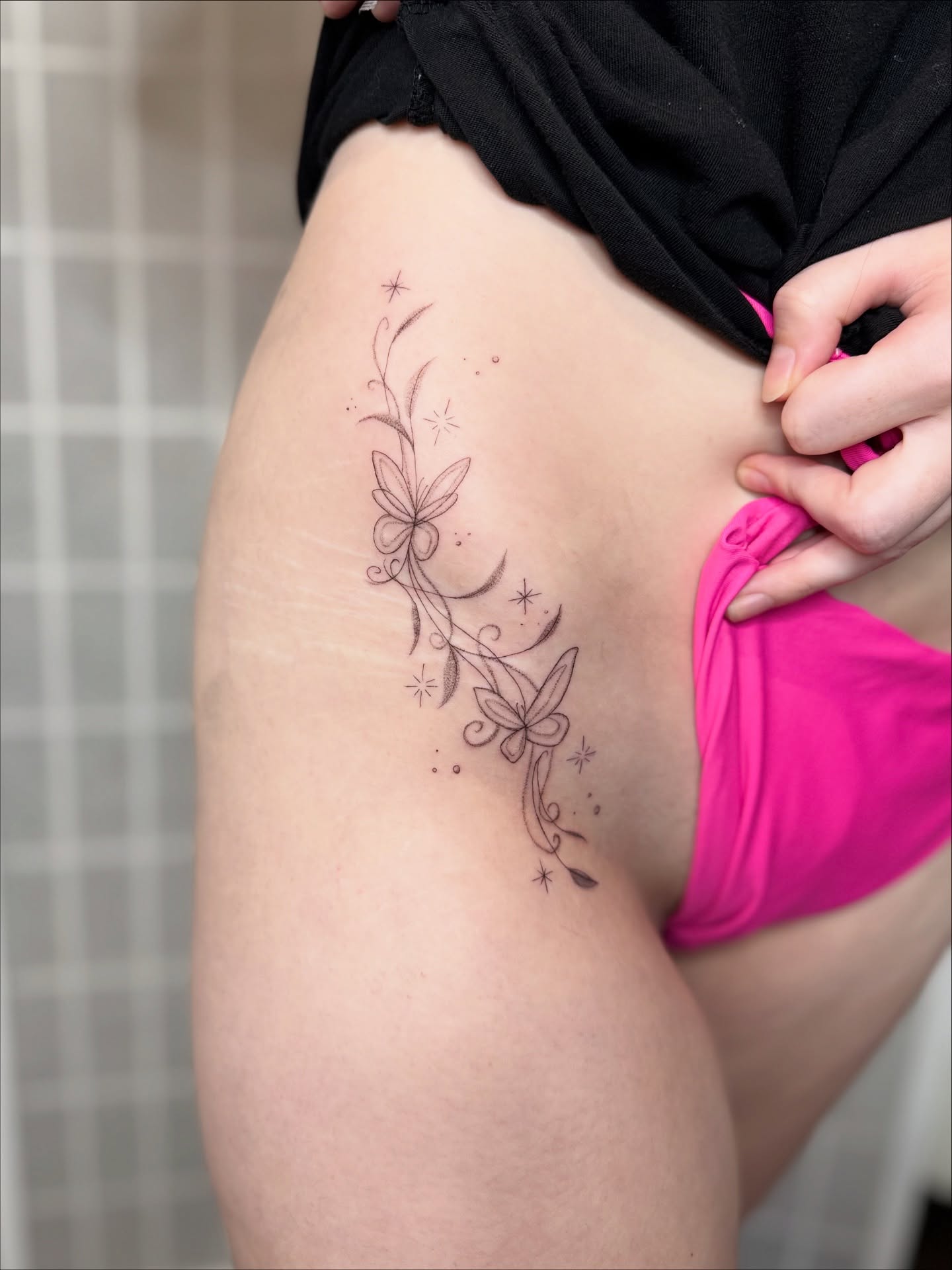 Butterfly and floral vine fine line tattoo on the thigh by Dama