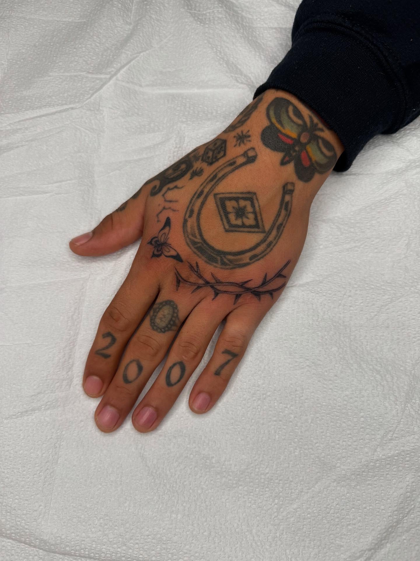Horseshoe and cross black and grey tattoo on the hand by Finley Jordan