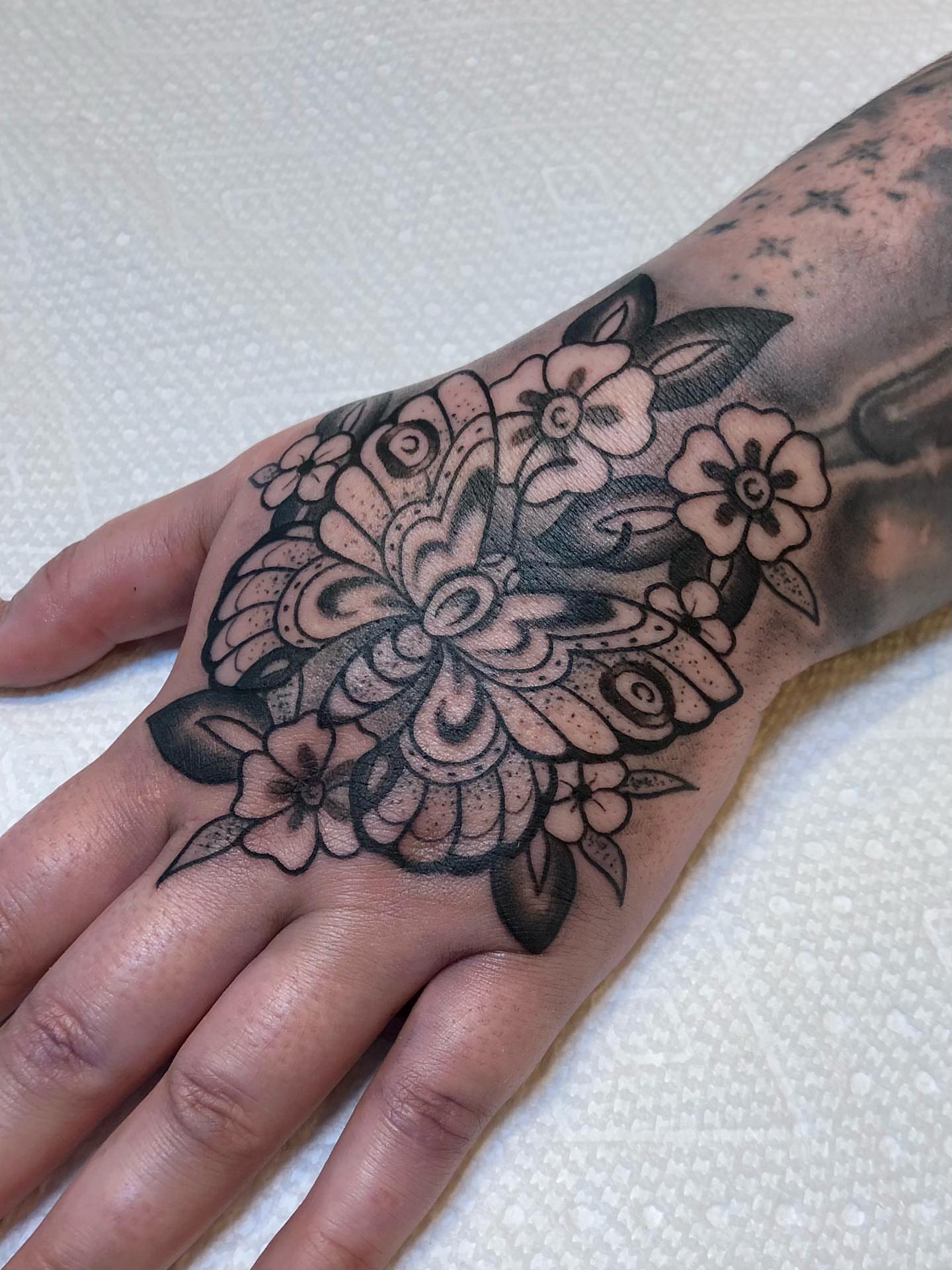 Butterfly and flowers black and grey tattoo on the hand by Leah Leinani