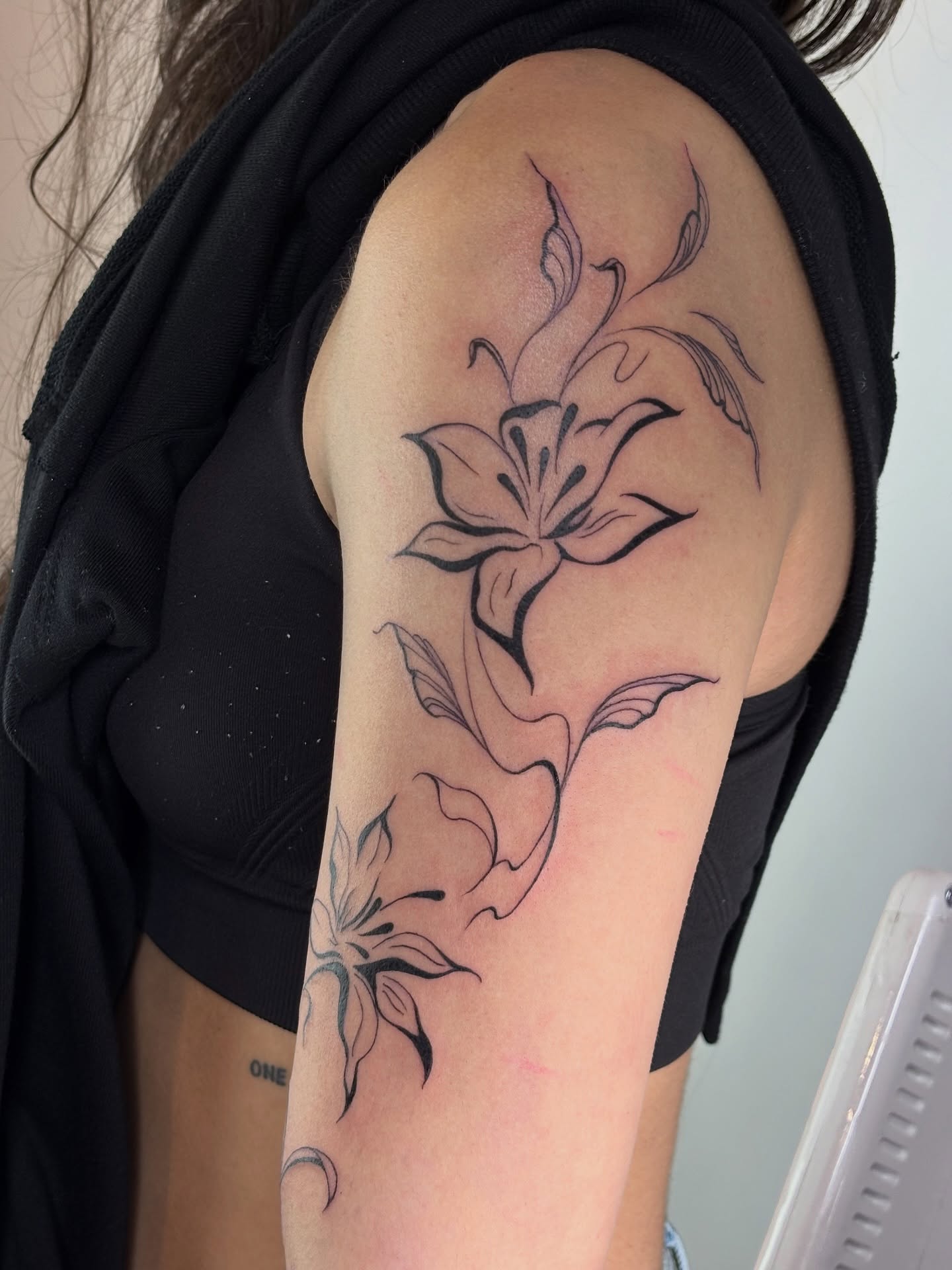 Lily black and grey tattoo on the upper arm by Dani
