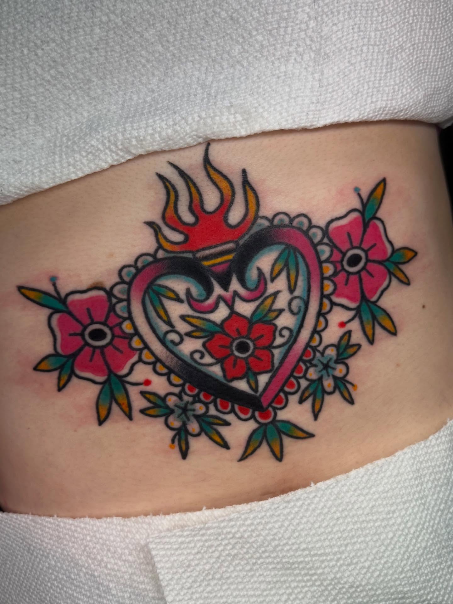 Heart with flames and flowers American traditional tattoo on the ribs by Shana