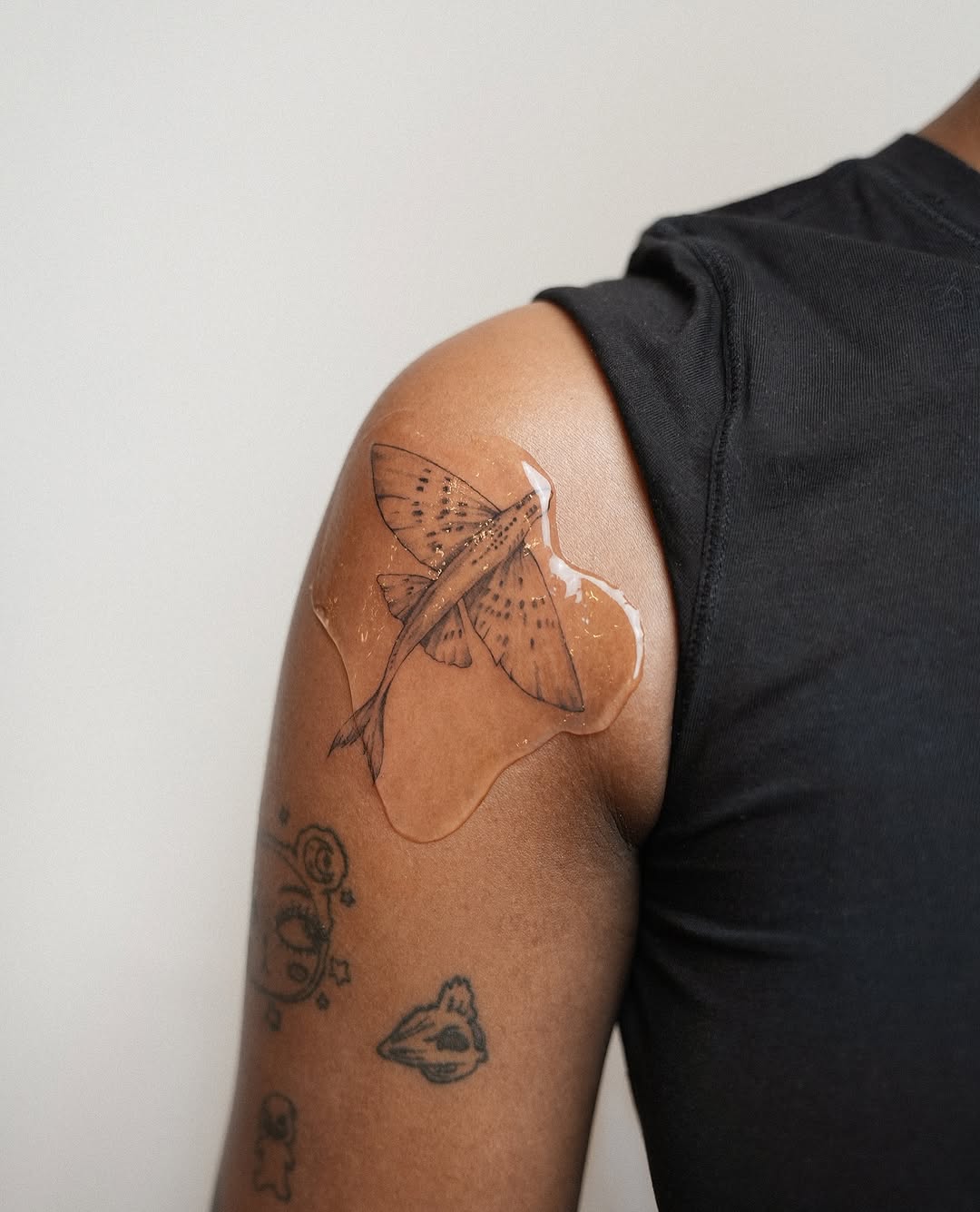 Flying fish fine line tattoo on the upper arm by Helly March