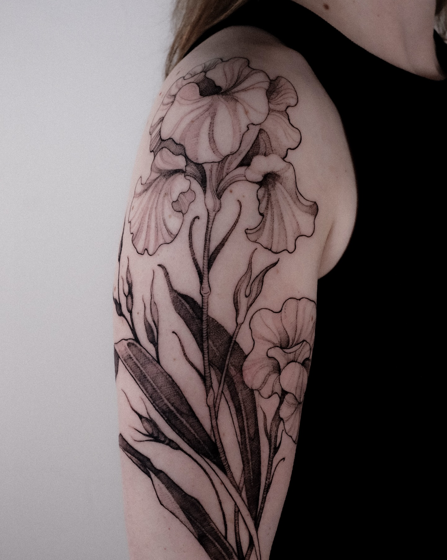Iris flowers black and grey tattoo on the upper arm by Alena Zozulenko