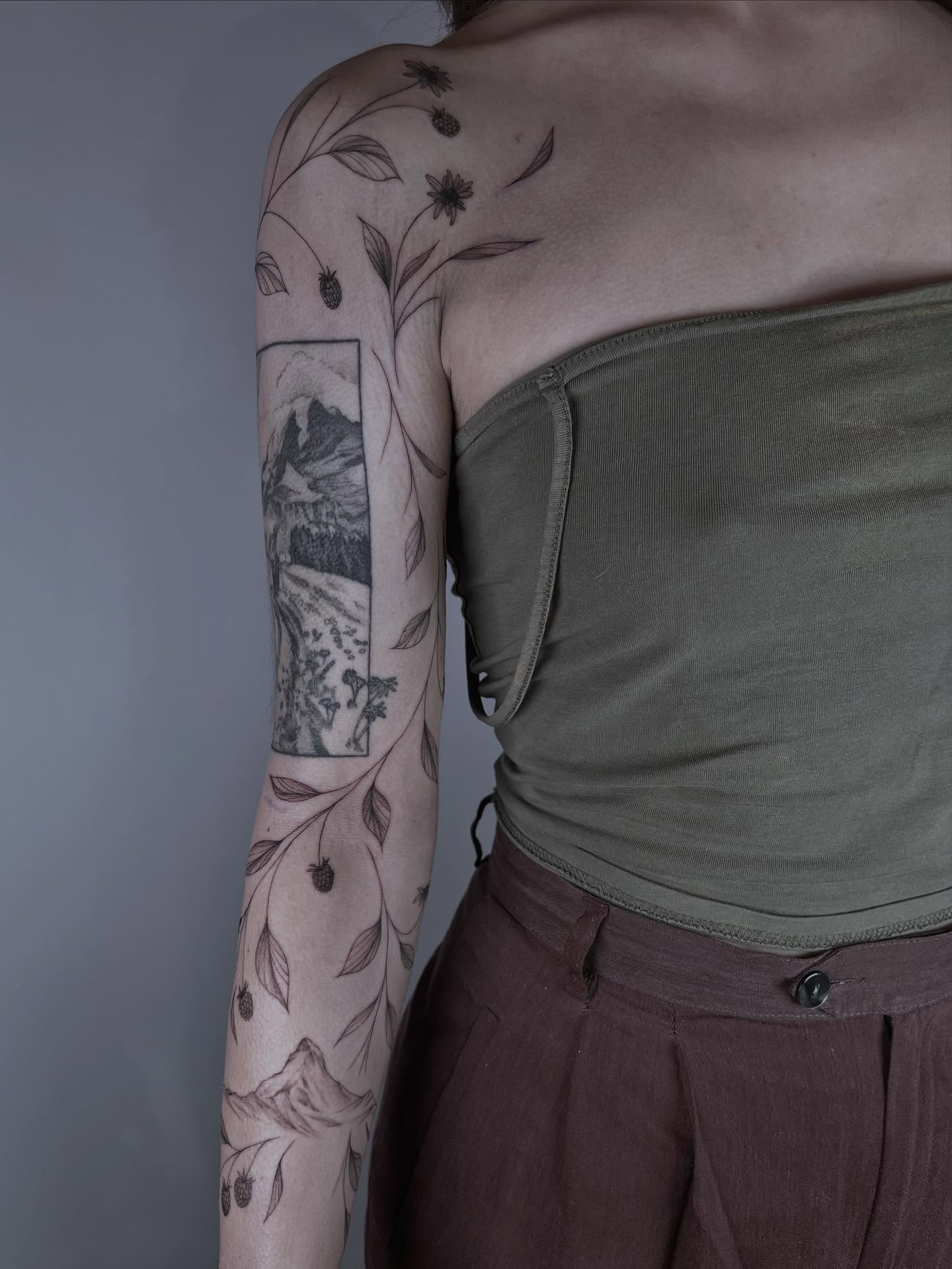 Landscape with flowers black and grey tattoo on the upper arm by Kite.Tattoo_Amber