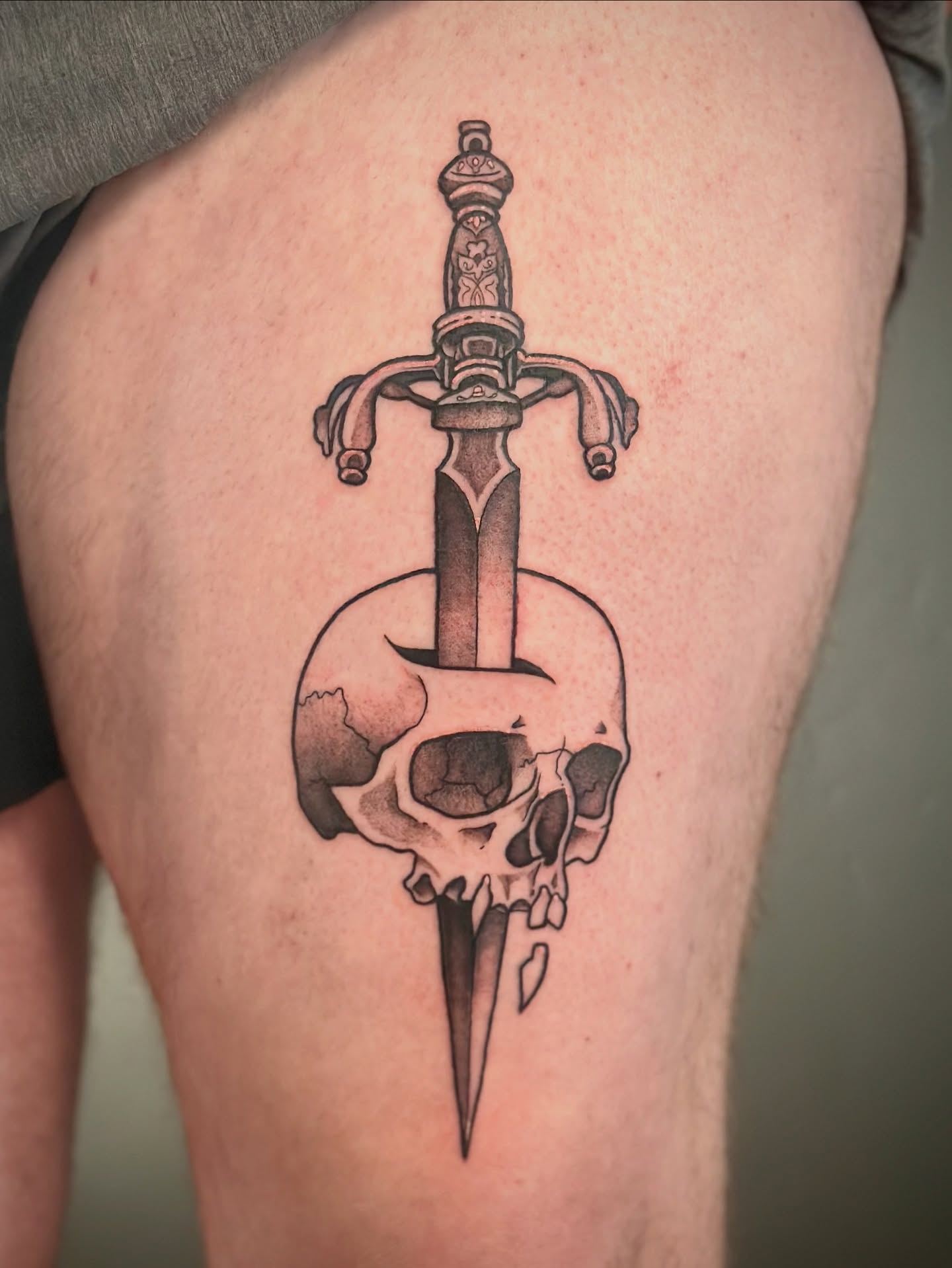 Sword through skull black and grey tattoo on the thigh by Maddie Morrill