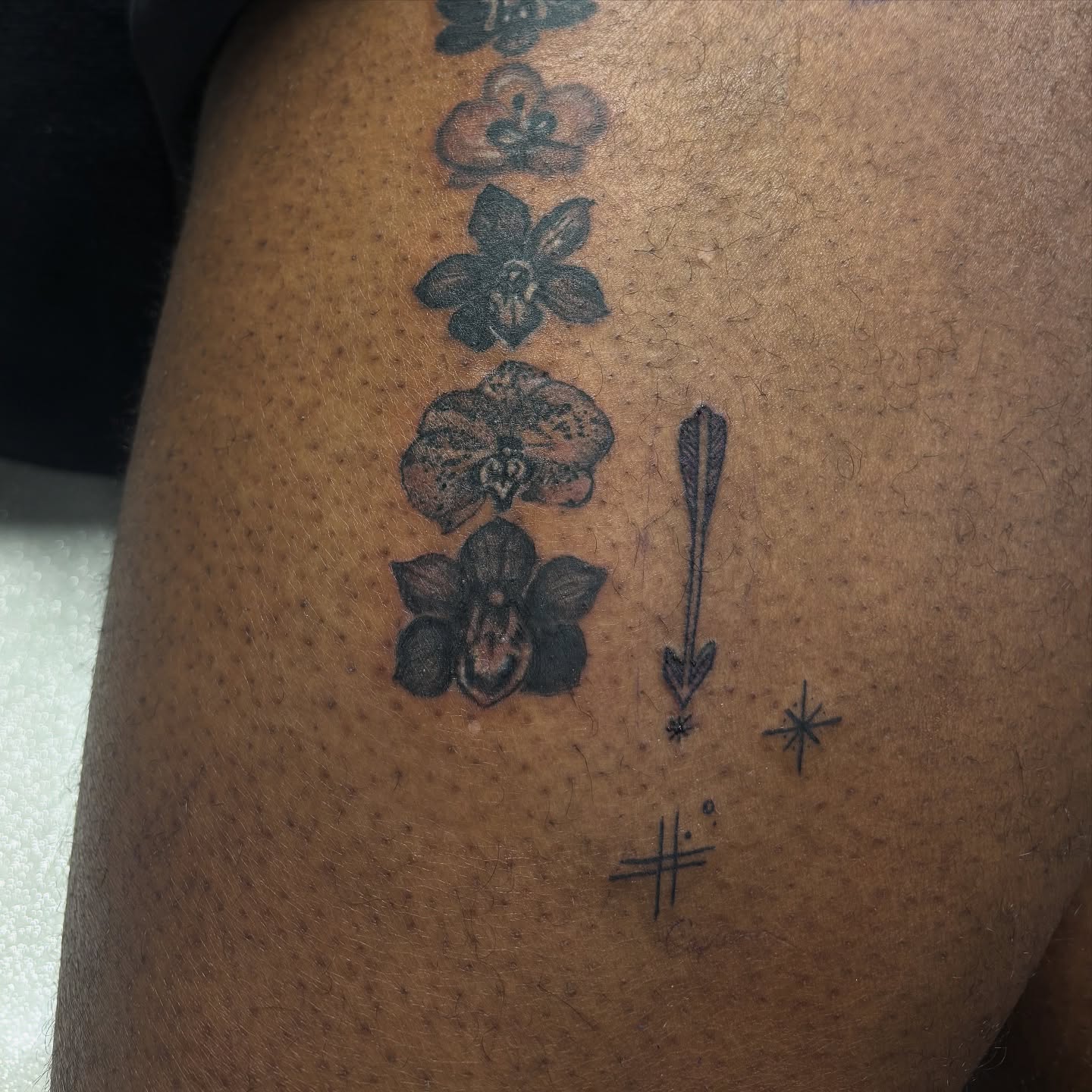 Orchids and arrow black and grey tattoo on the thigh by Rachel