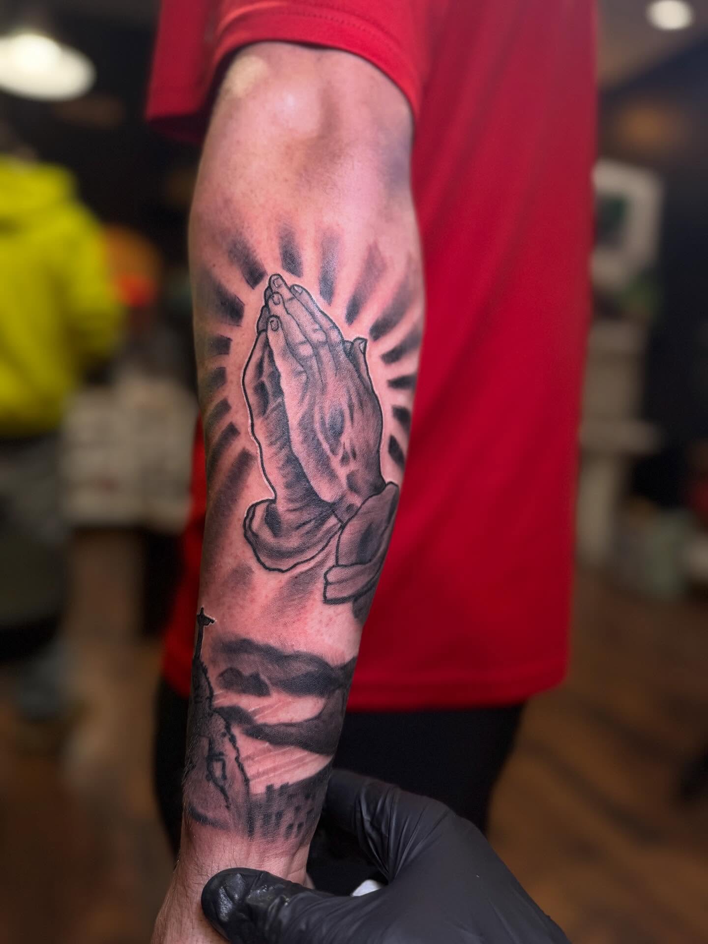 Praying hands black and grey tattoo on the forearm by Robbie Roberson