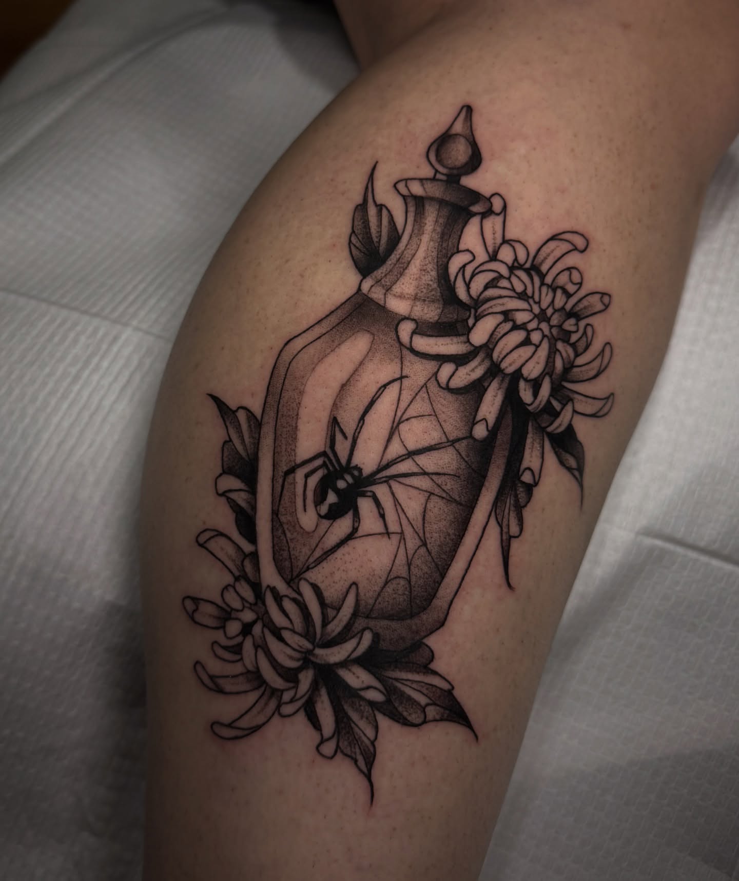 Perfume bottle with flowers realism tattoo on the thigh by Lauren Peltz