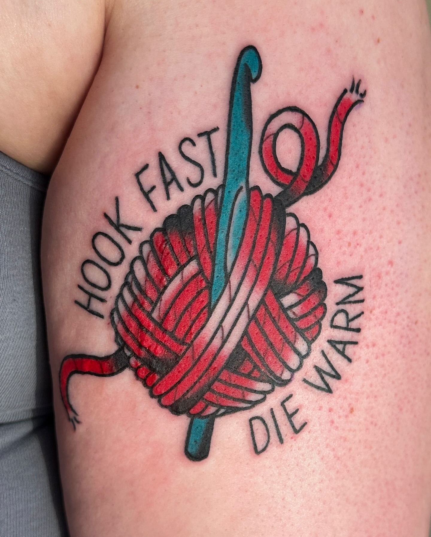 Crochet hook and yarn neo-traditional tattoo on the upper arm by Paige Ochoa