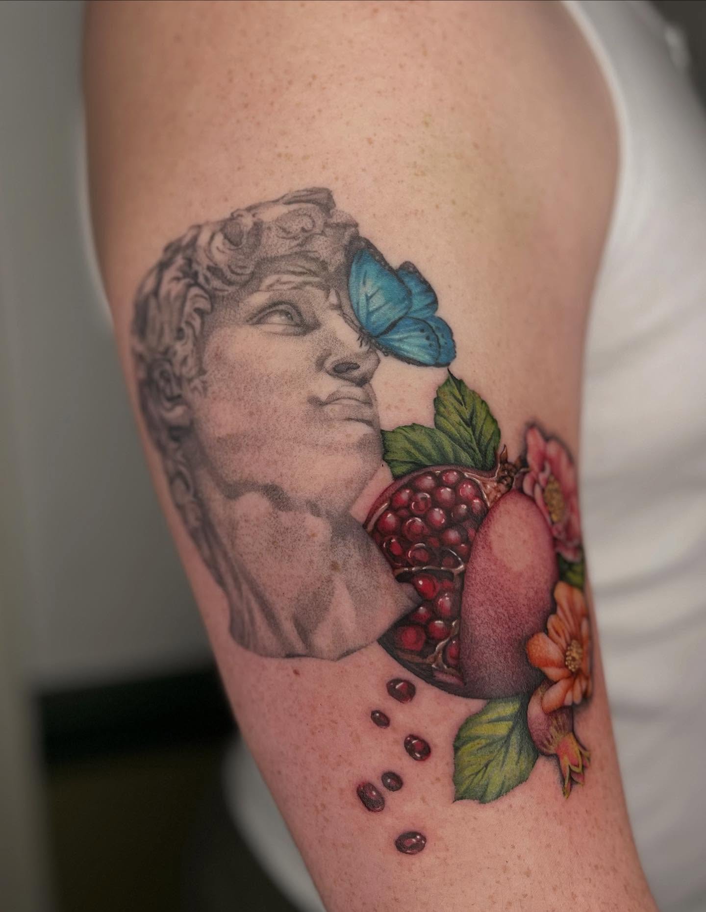 Statue head with pomegranate realism tattoo on the thigh by Ash F