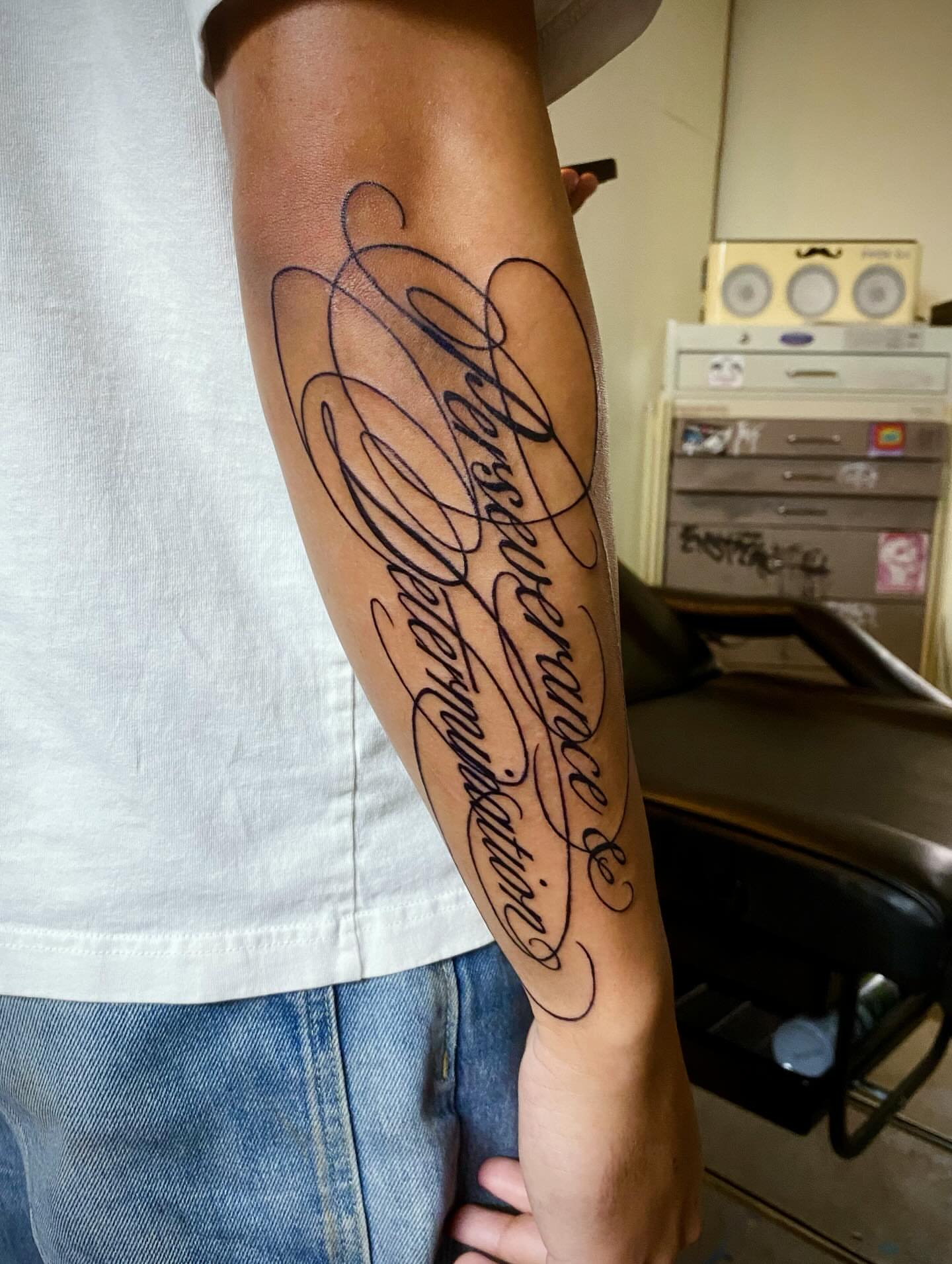 Perseverance & determination lettering script tattoo on the forearm by Quin Walker