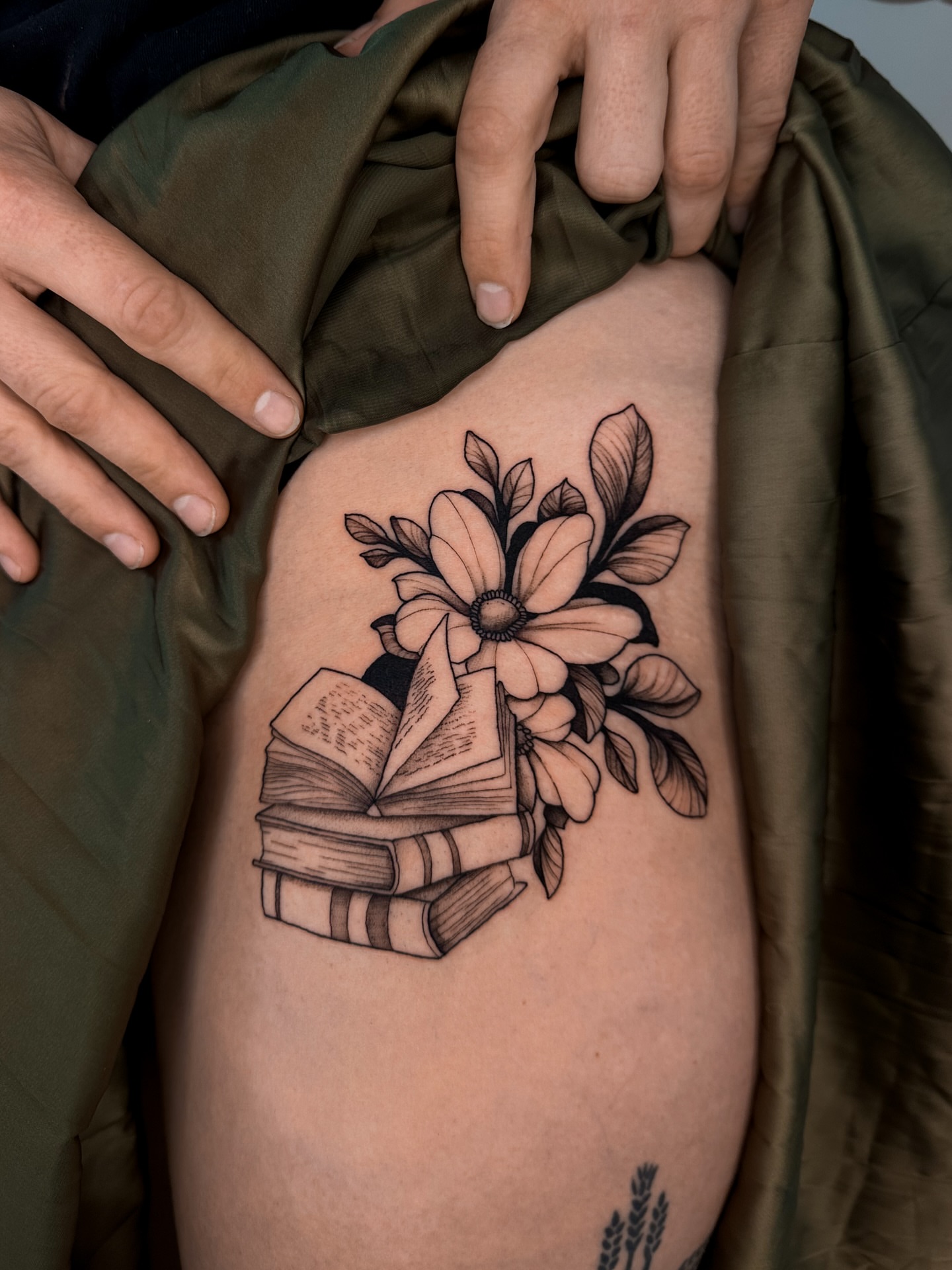 Book and flower bouquet black and grey tattoo on the thigh by Lauren