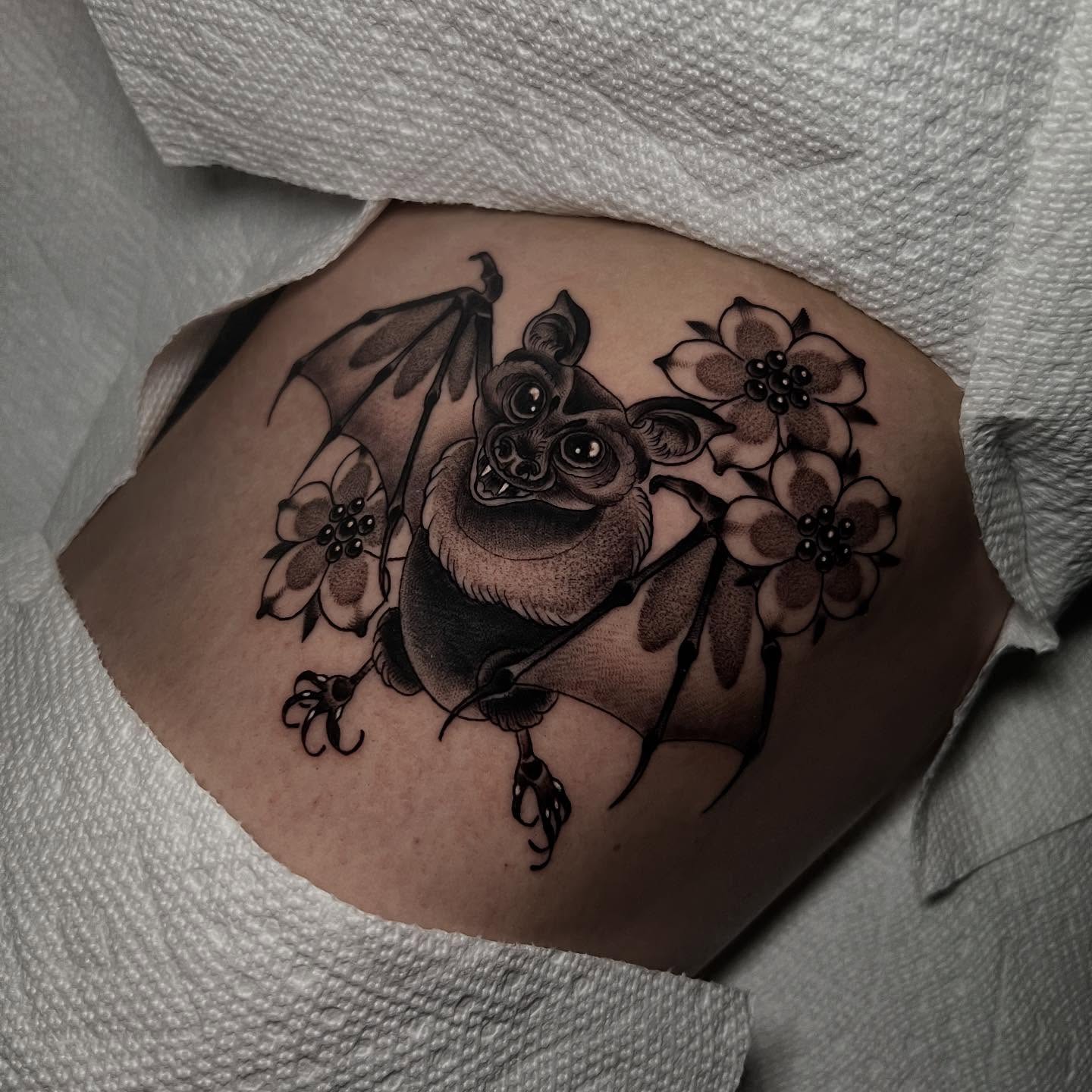 Bat and flowers black and grey tattoo on the torso by Katie Ann Tattoos