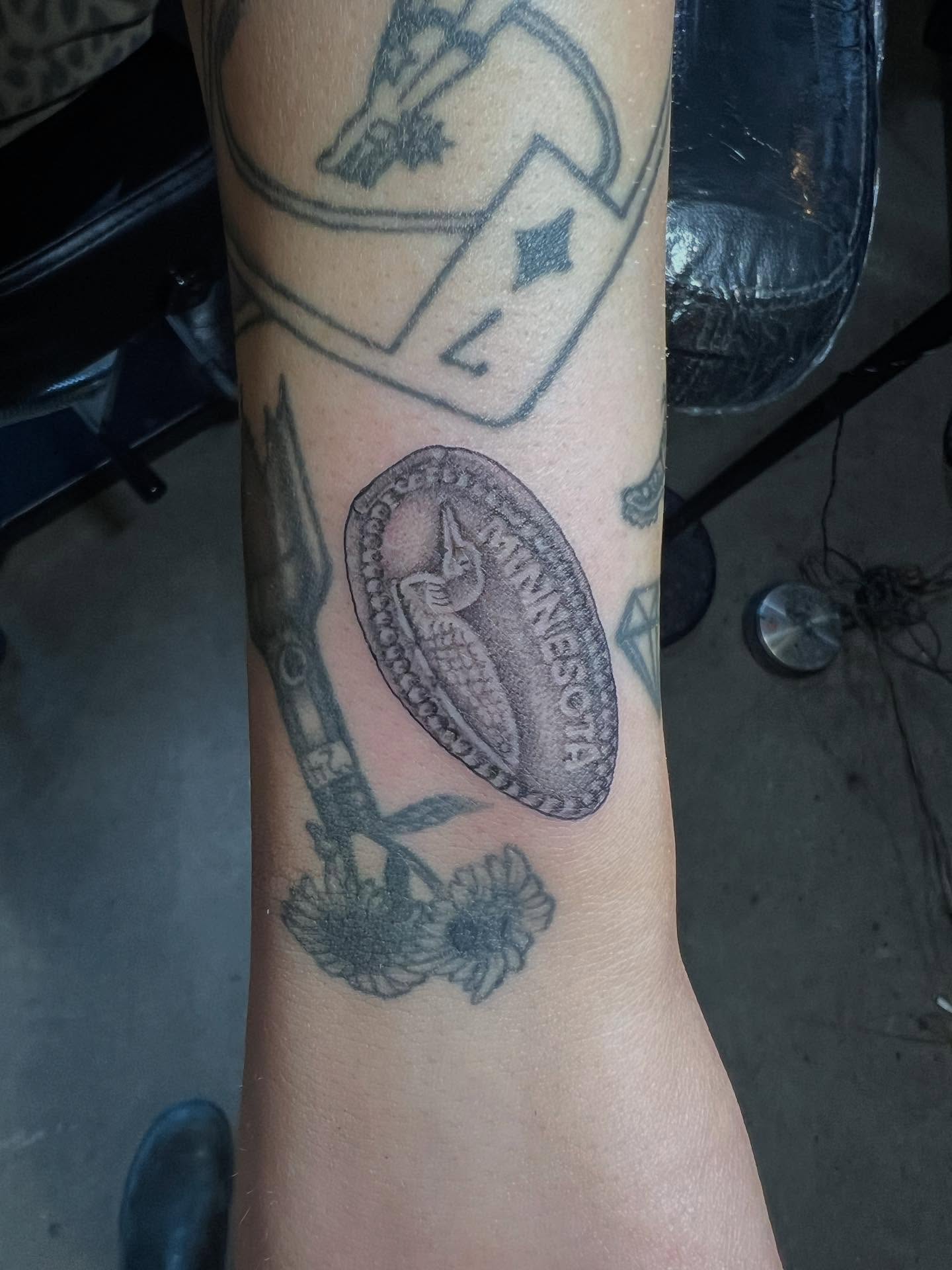 State seal and sunflowers black and grey tattoo on the forearm by Siërra Nicole, Minneapolis, Minnesota