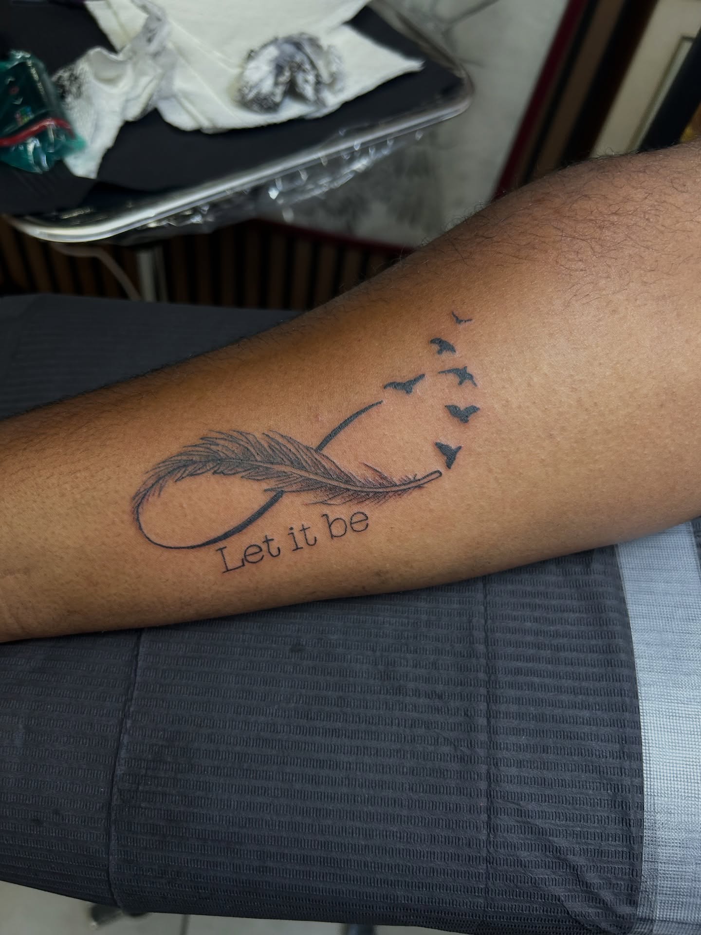 Feather and infinity symbol black and grey tattoo on the forearm by Torrey, Austin, Texas