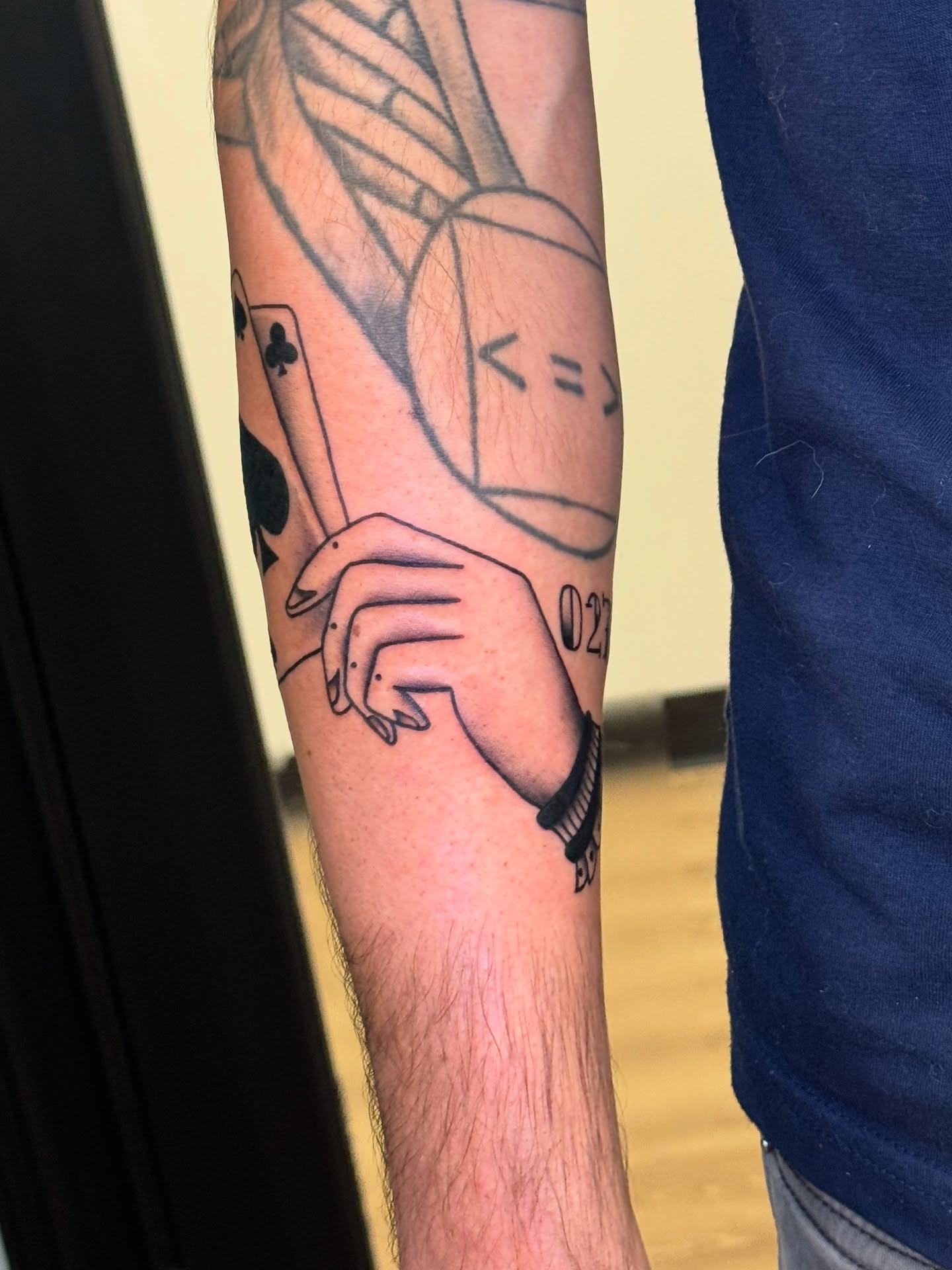 Hand holding playing card black and grey tattoo on the forearm by Madison Pegram