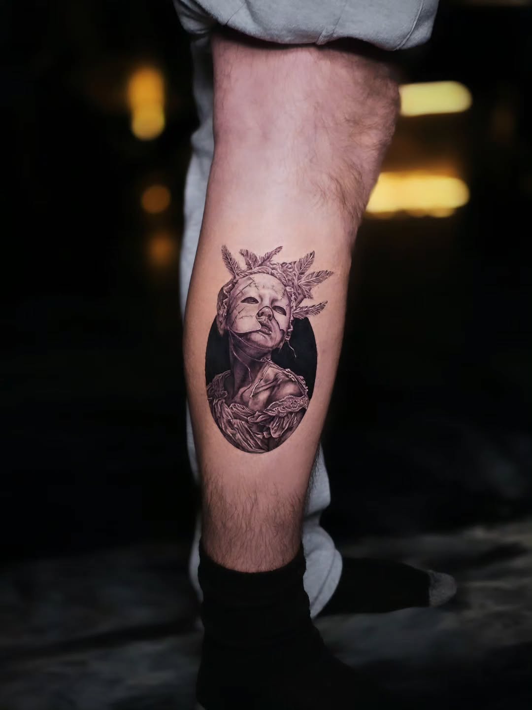 Woman with mask and feathers surrealism tattoo on the calf by Jake Barney