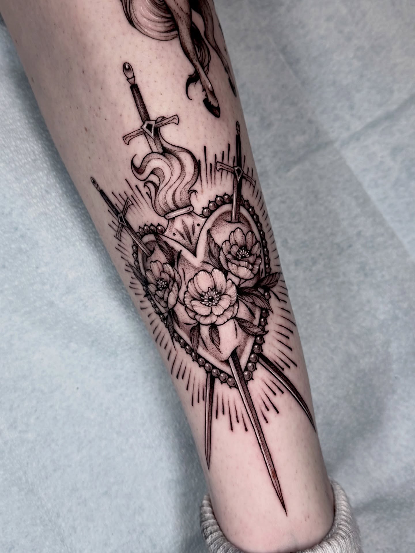 Heart with flowers and swords black and grey tattoo on the forearm by Kathryn Semus