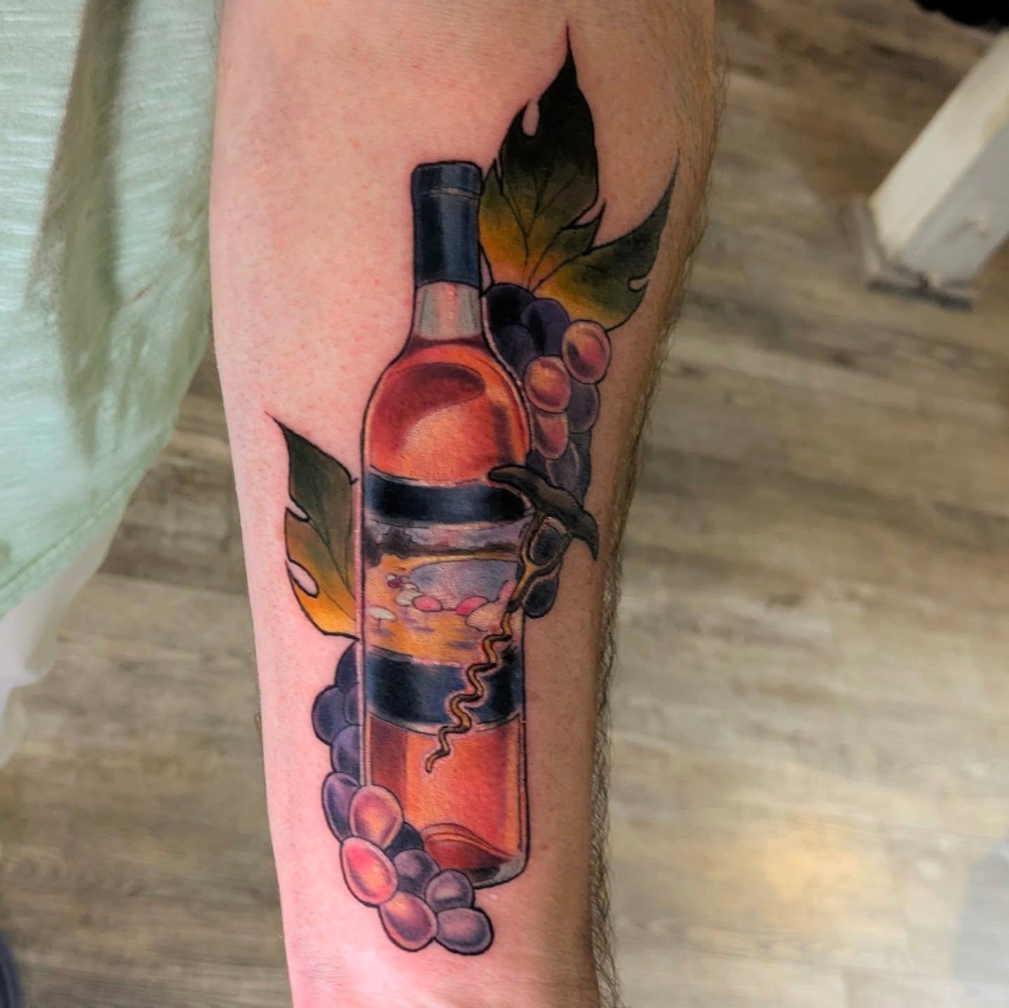 Wine bottle and grapes realism tattoo on the forearm by Lahel (Lay-el) Fowler