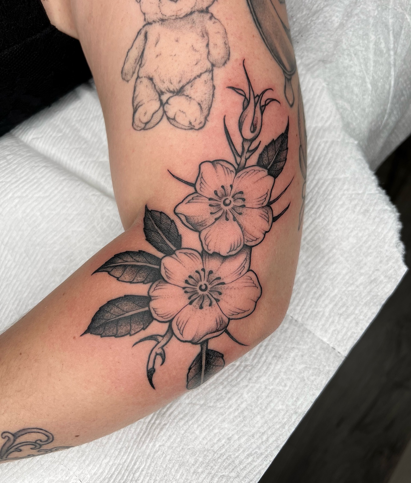 Flowers and teddy bear black and grey tattoo on the forearm by 𝔐𝔦𝔠𝔥𝔢𝔩𝔩𝔢 ℭ𝔥𝔞𝔪𝔢𝔯𝔩𝔦𝔨