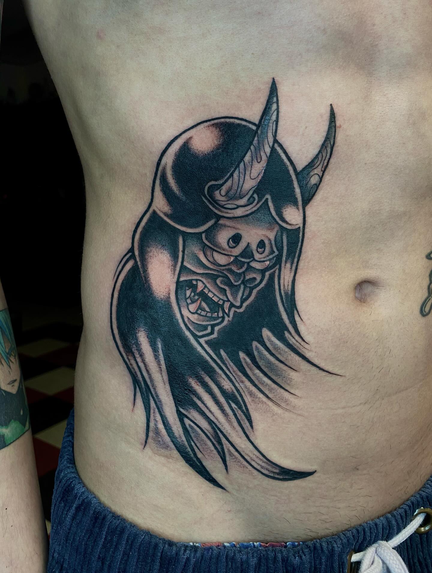 Demon mask black and grey tattoo on the ribs by Jonah