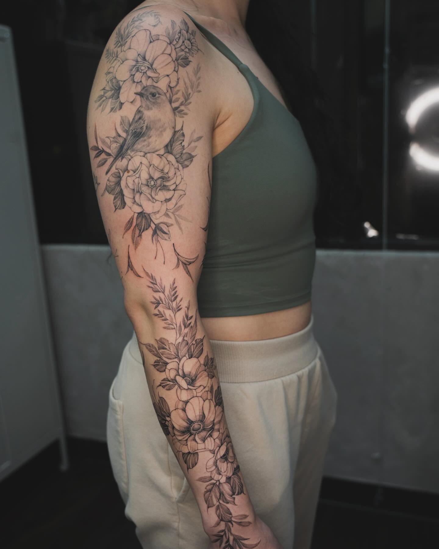 Floral bouquet with bird black and grey tattoo on the upper arm by Tri
