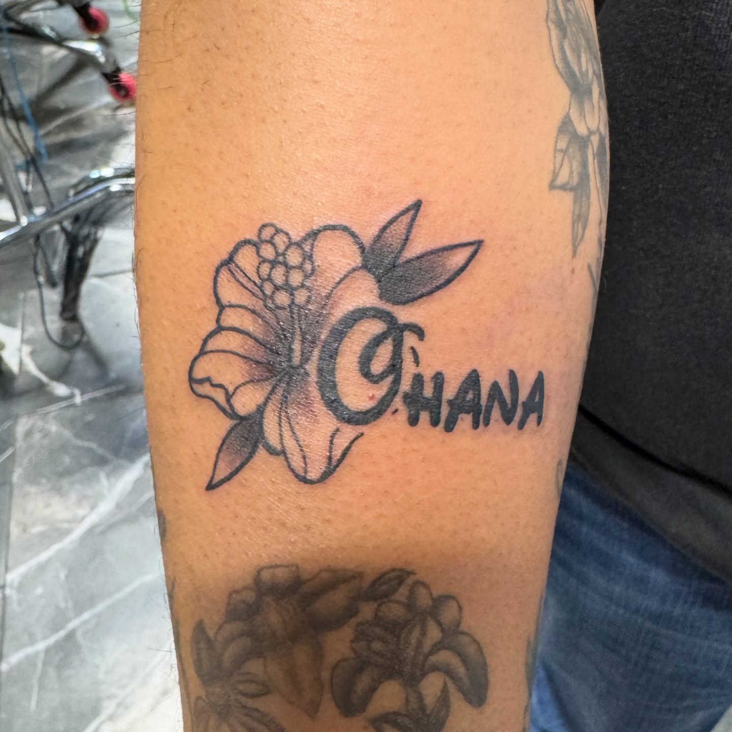 Hawaiian flower and script black and grey tattoo on the forearm by Sonder