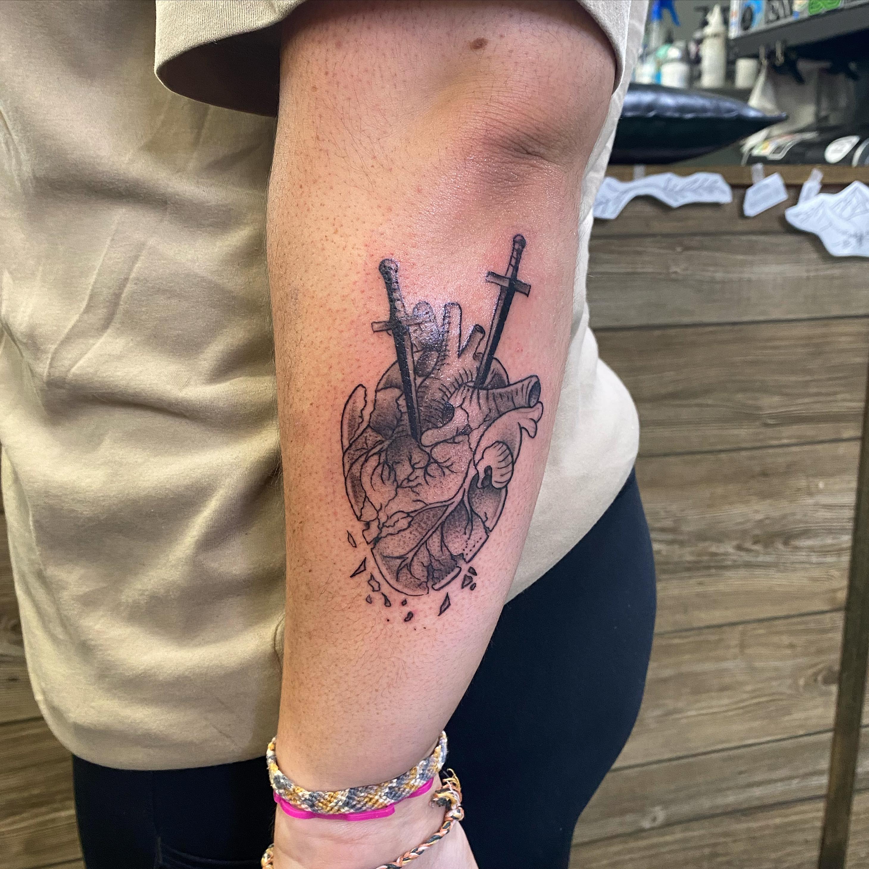 Heart with swords black and grey tattoo on the forearm by Spencer Jones Tattoos