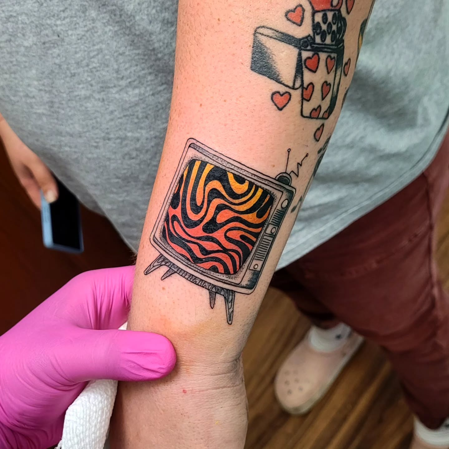 Flame-patterned television American traditional tattoo on the forearm by Wray Saulsberry