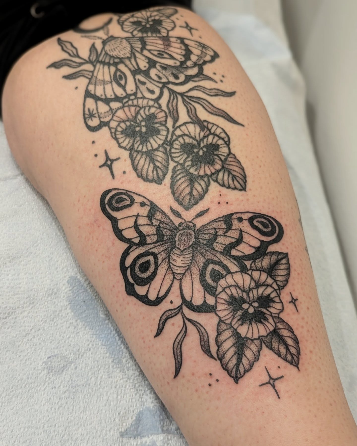 Butterfly and flowers black and grey tattoo on the thigh by Dani Harkey