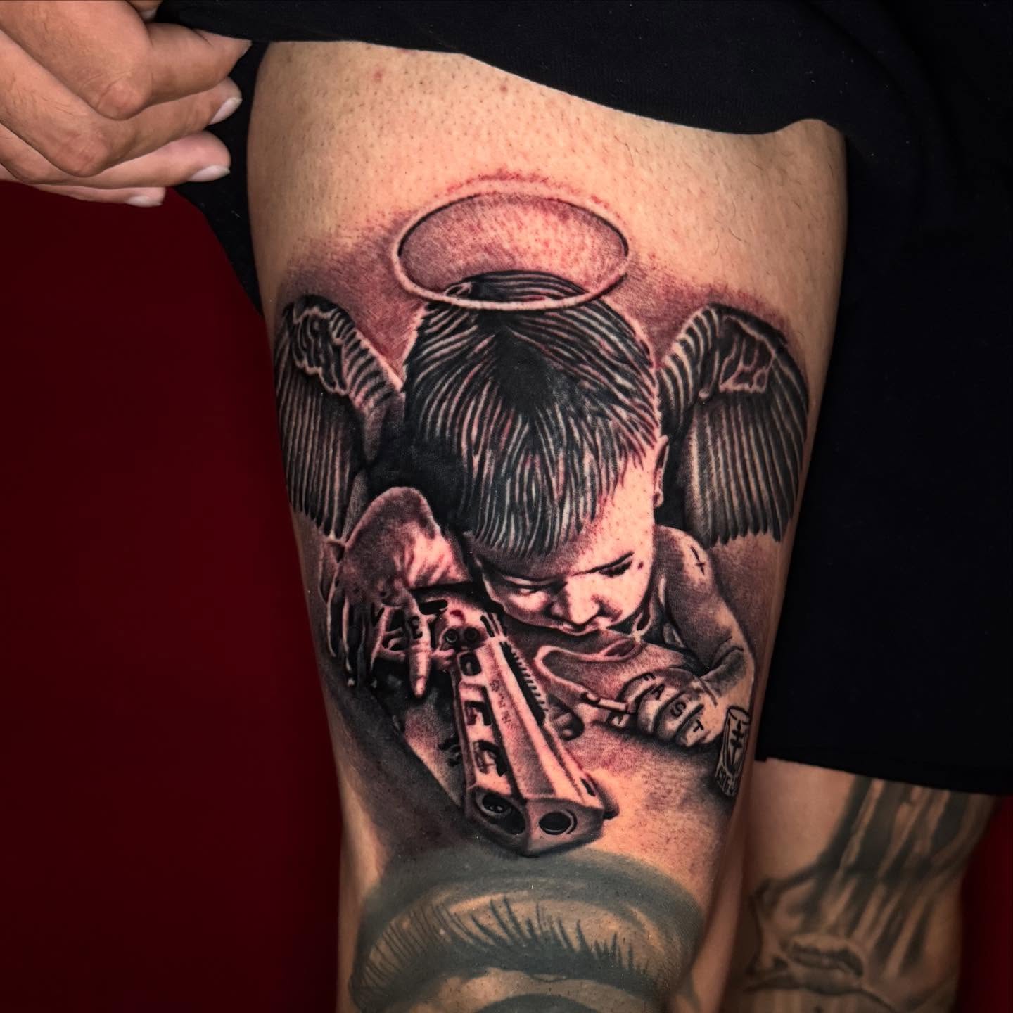 Child with halo and gun realism tattoo on the thigh by Jayb, Passaic, New Jersey