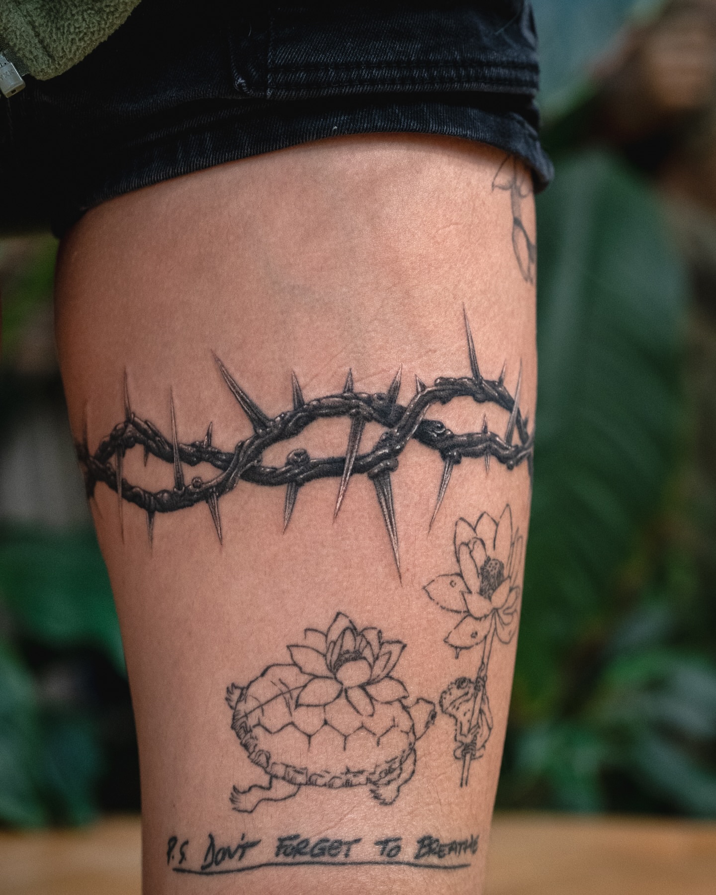 Crown of thorns and lotus flowers black and grey tattoo on the thigh by James Fernella, San Francisco, California