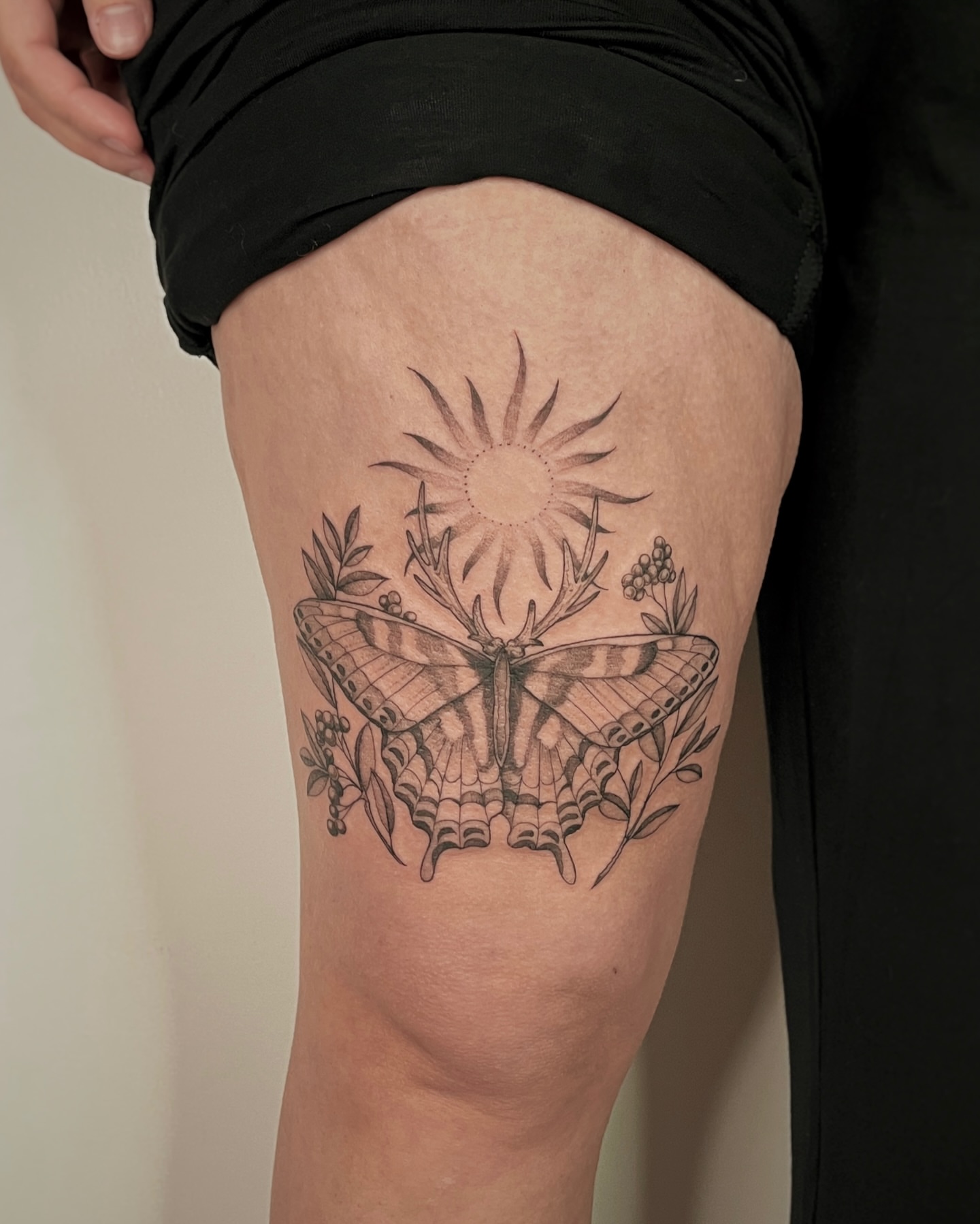 Butterfly and sun black and grey tattoo on the thigh by Mikayla Sue