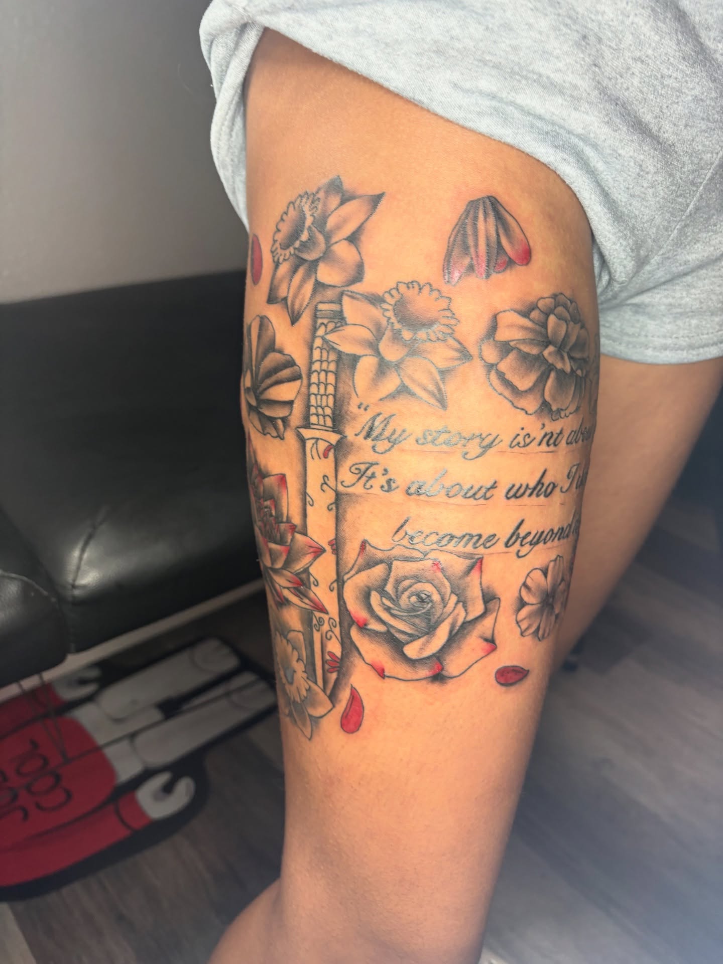 Flowers and quote black and grey tattoo on the thigh by Maleek Inkz