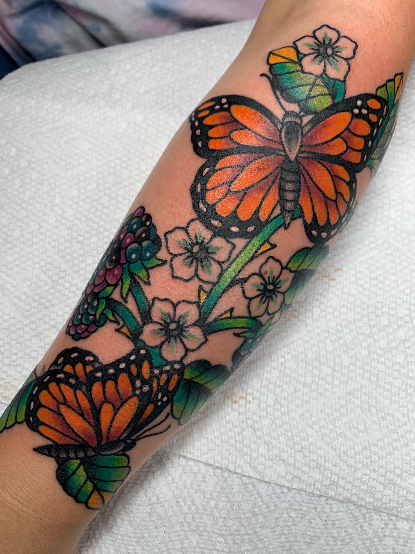 Monarch butterflies and flowers American traditional tattoo on the forearm by April Morris ⚔️ Tattoo Goblin