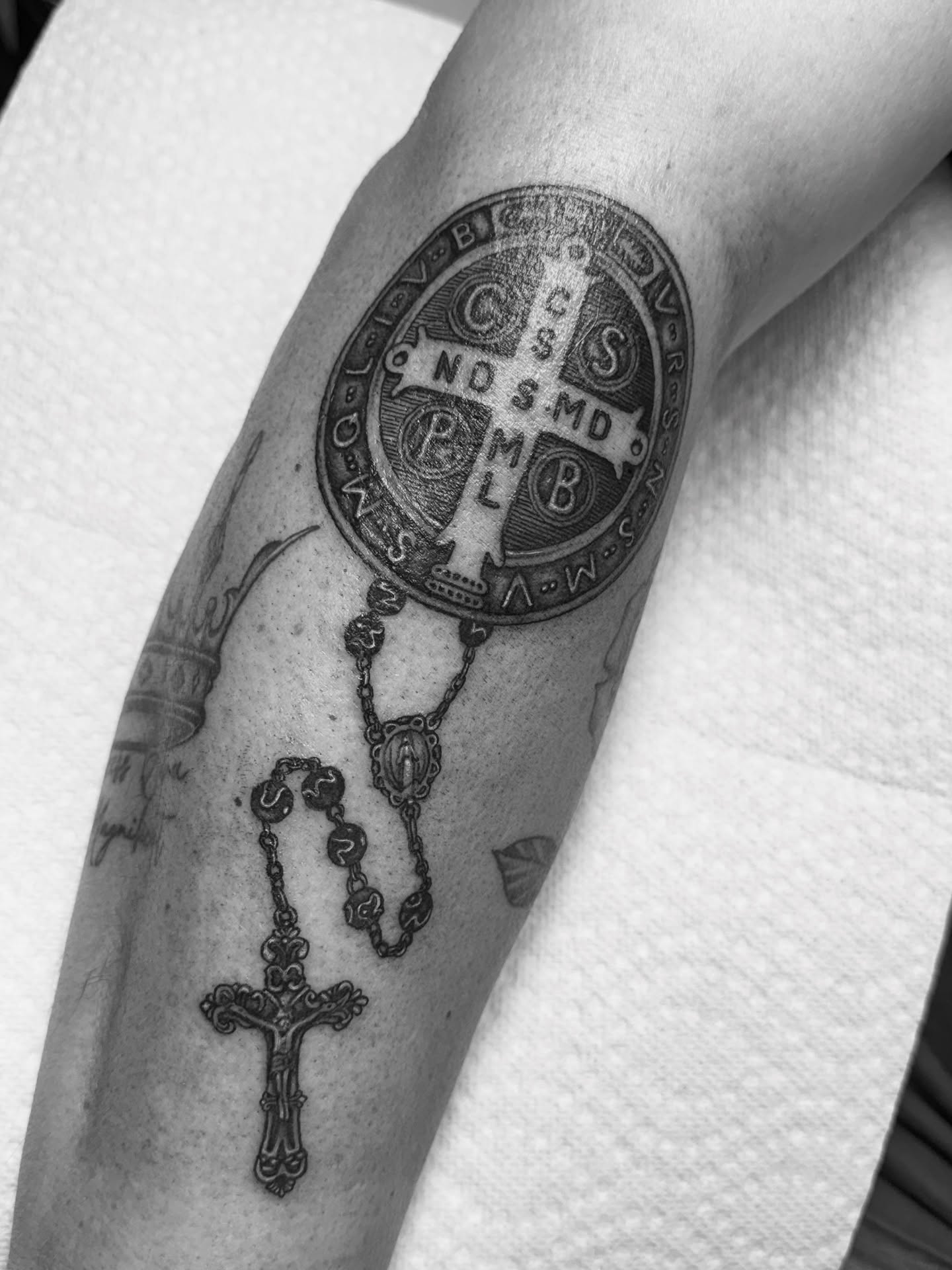 Religious medallion and rosary black and grey tattoo on the forearm by Eva, Matawan, New Jersey