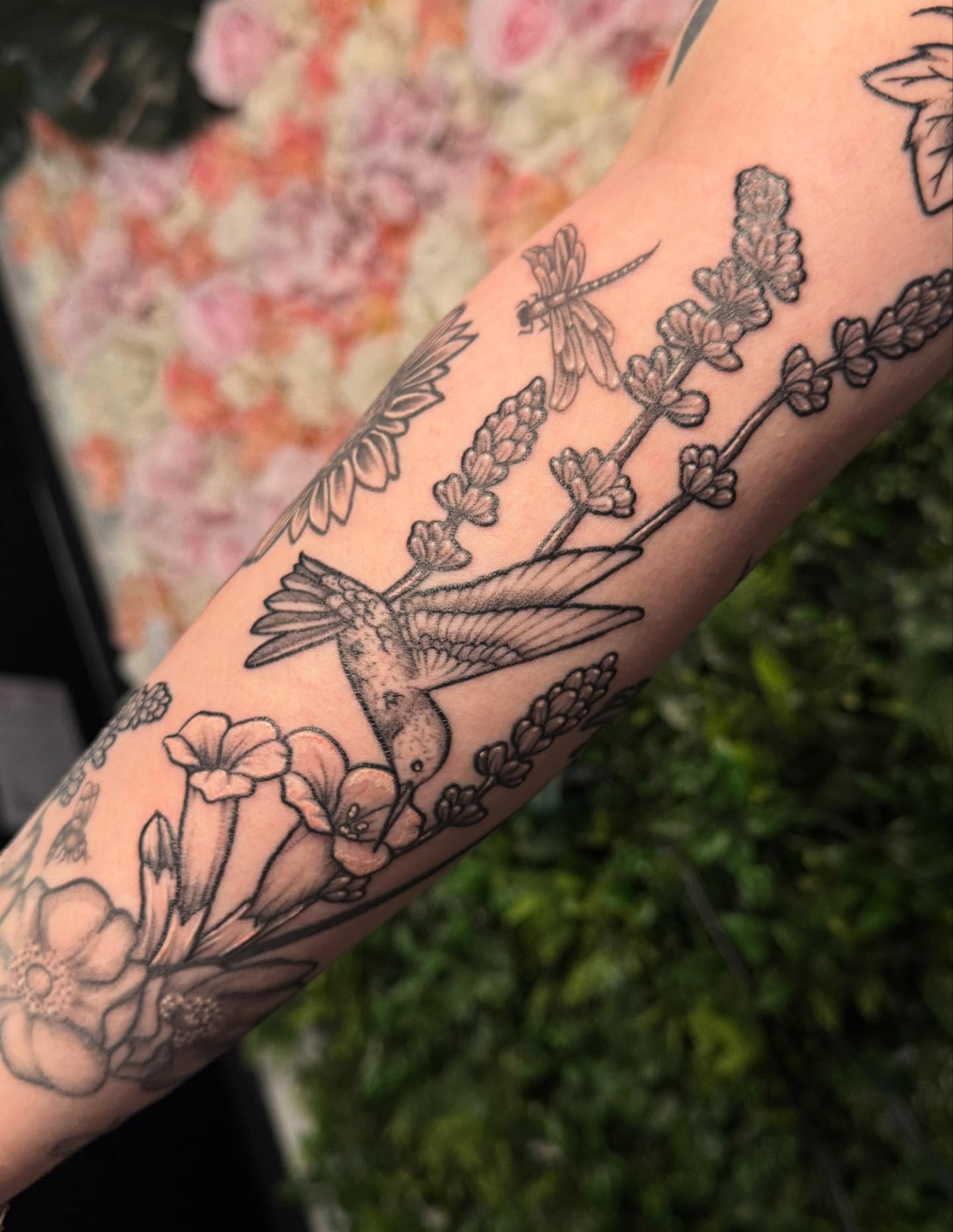 Hummingbird and flowers black and grey tattoo on the forearm by Ember