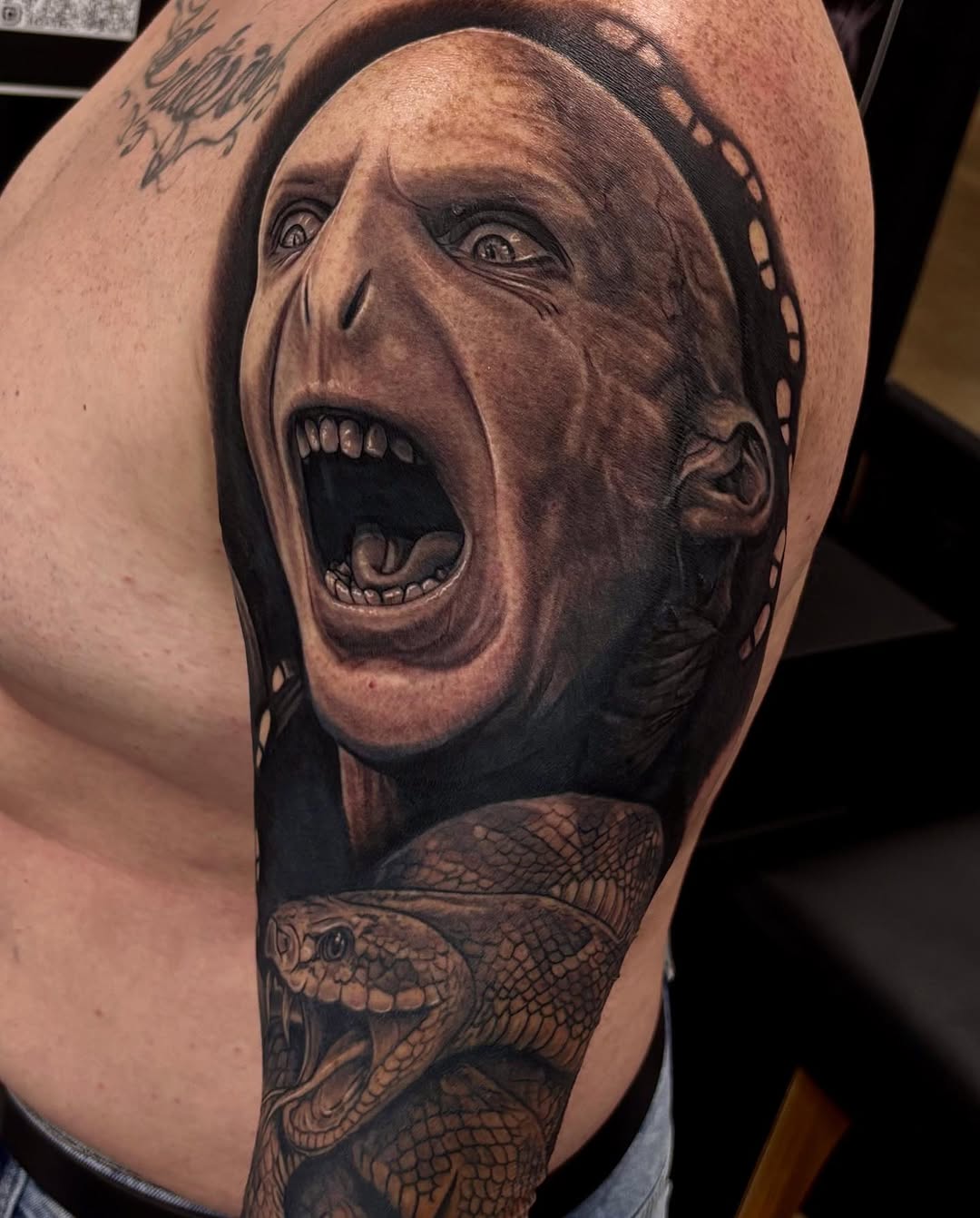 Voldemort screaming with a snake realism tattoo on the upper arm by Jayden A