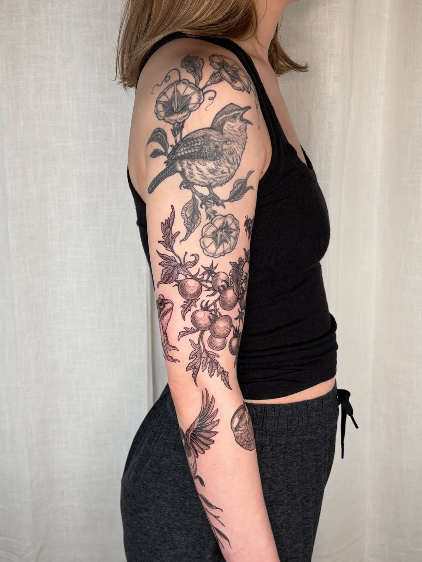 Bird and floral black and grey tattoo on the upper arm by Maggie
