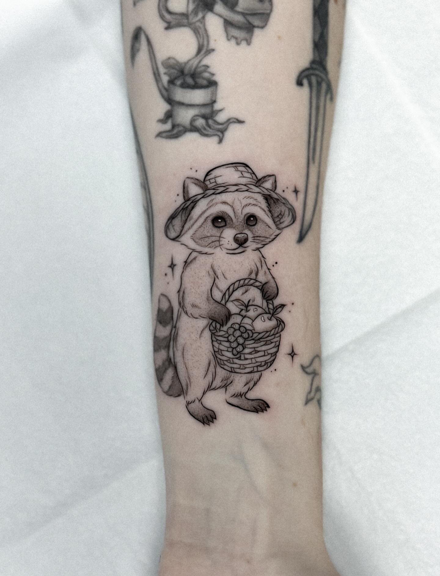 Raccoon with basket realism tattoo on the forearm by Whimsical Tattoos