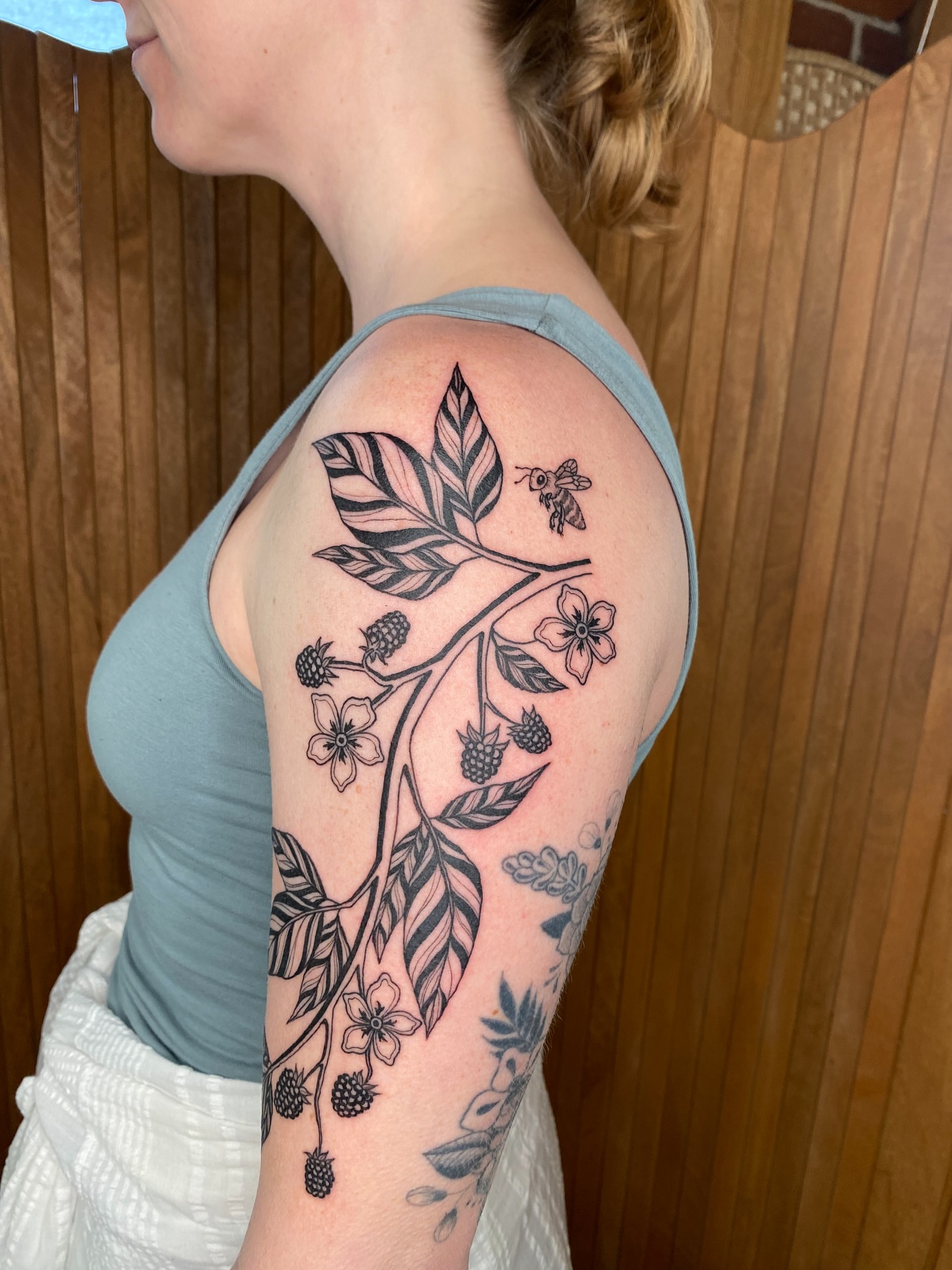 Branch with flowers and berries black and grey tattoo on the upper arm by Avery Kane