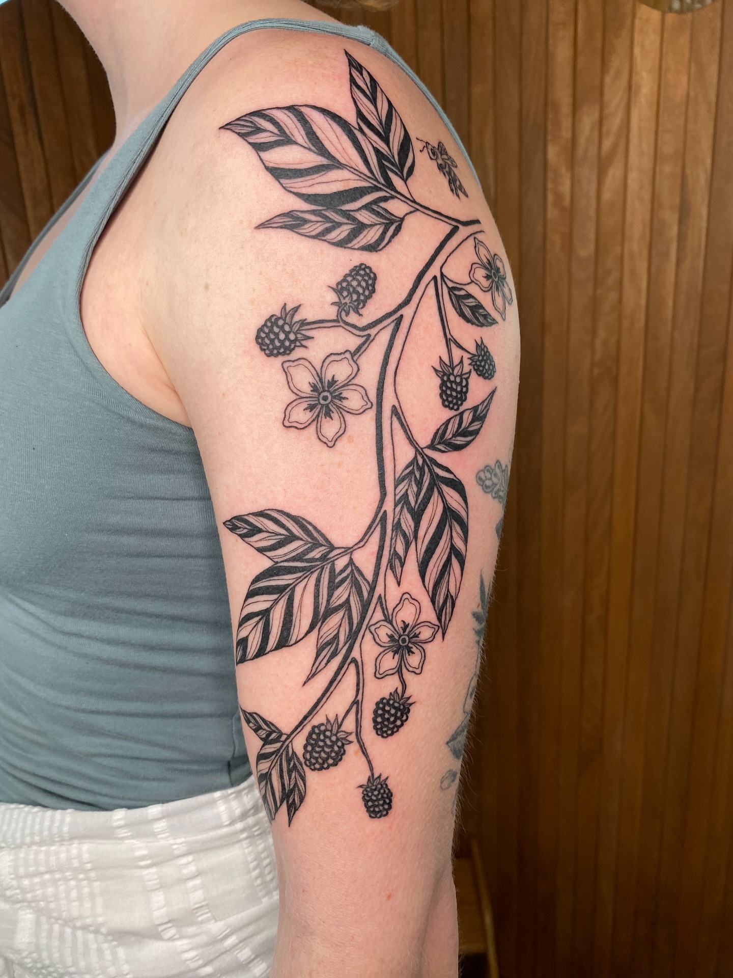 Berry bush black and grey tattoo on the upper arm by Avery Kane