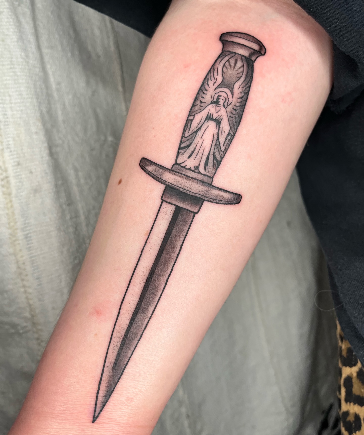 Sword with angel black and grey tattoo on the forearm by Maris Hare, Philadelphia, Pennsylvania